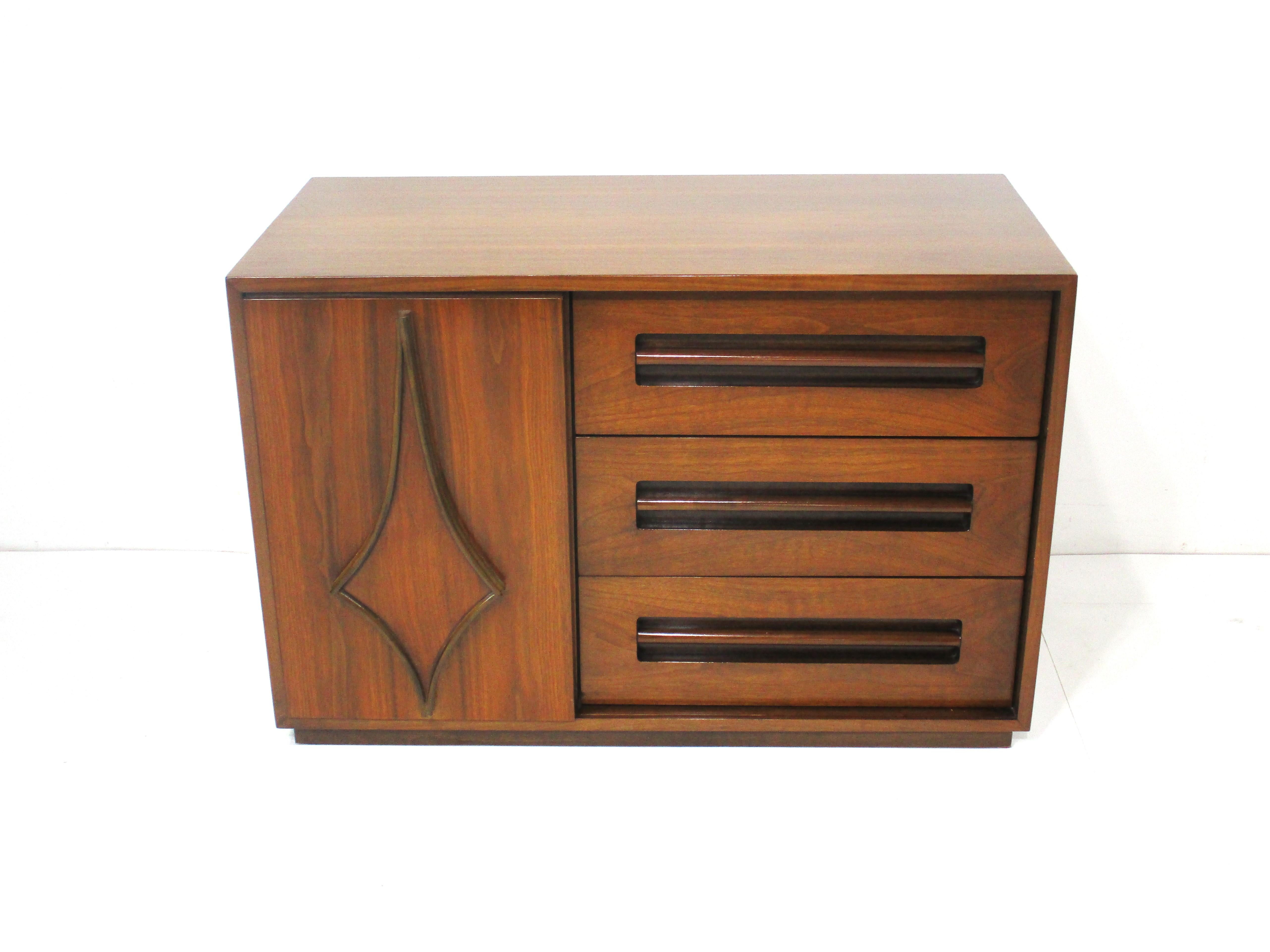 A smaller scaled walnut credenza cabinet with one sliding door and sculptural design to the front . Three small drawers behind the door and to the other side three drawers with long handles having hidden finger pull grooves . Sitting on a lower kick