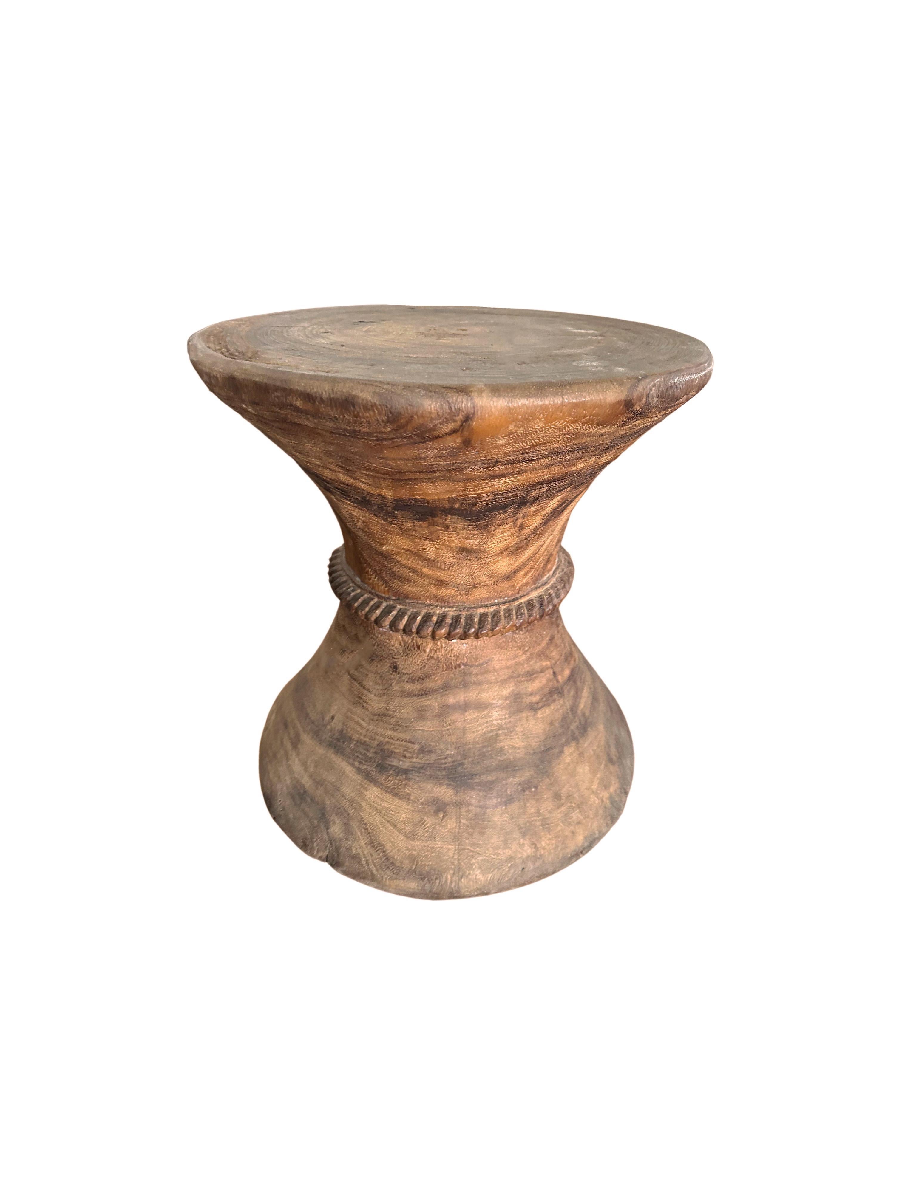 A wonderfully sculptural solid teak side table with carved detailing at its center. The mix of wood textures and shades add to its charm. 
