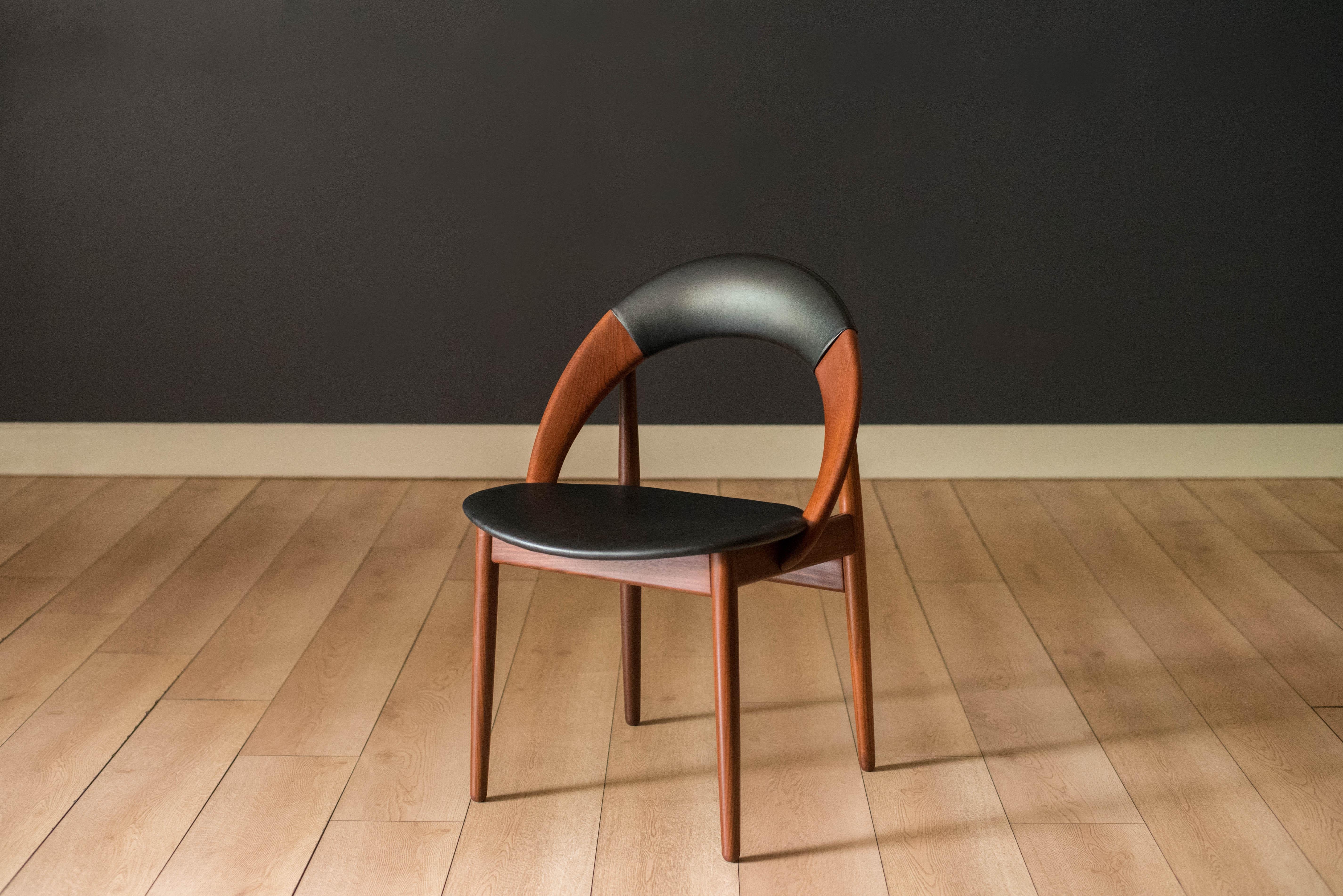 Mid century modern dining chair in solid teak designed by Arne Hovmand Olsen for Mogens Kold, circa 1960's. This unique side chair features a sculptural hoop shaped backrest in a black leatherette fabric supported by tapered pencil legs. The perfect