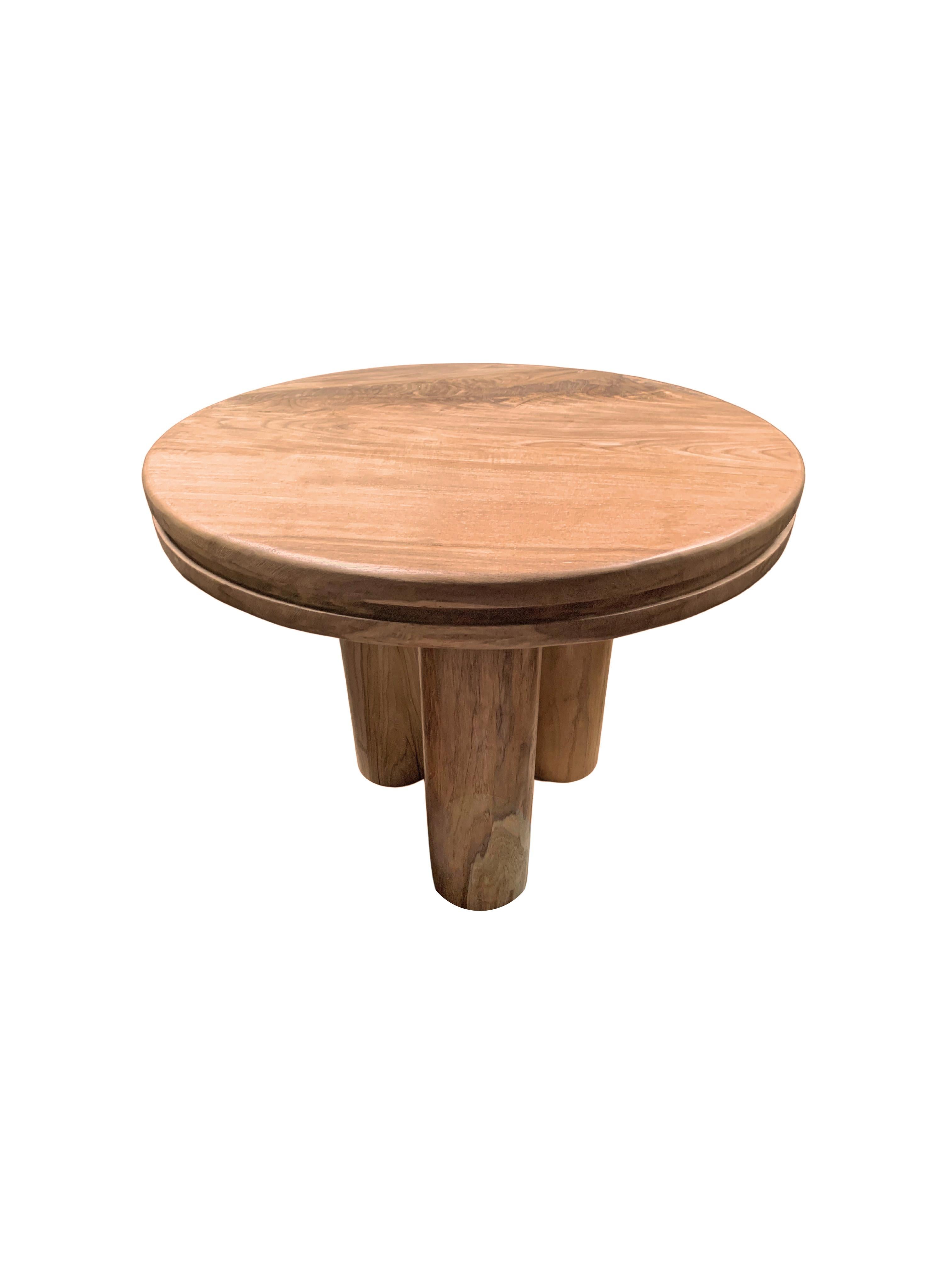 A wonderfully sculptural round side table. Crafted from solid teak wood the table top features a carved channel that wraps around its circumference. The table features three cylindrical legs. The wood textures and shades throughout add to its charm.