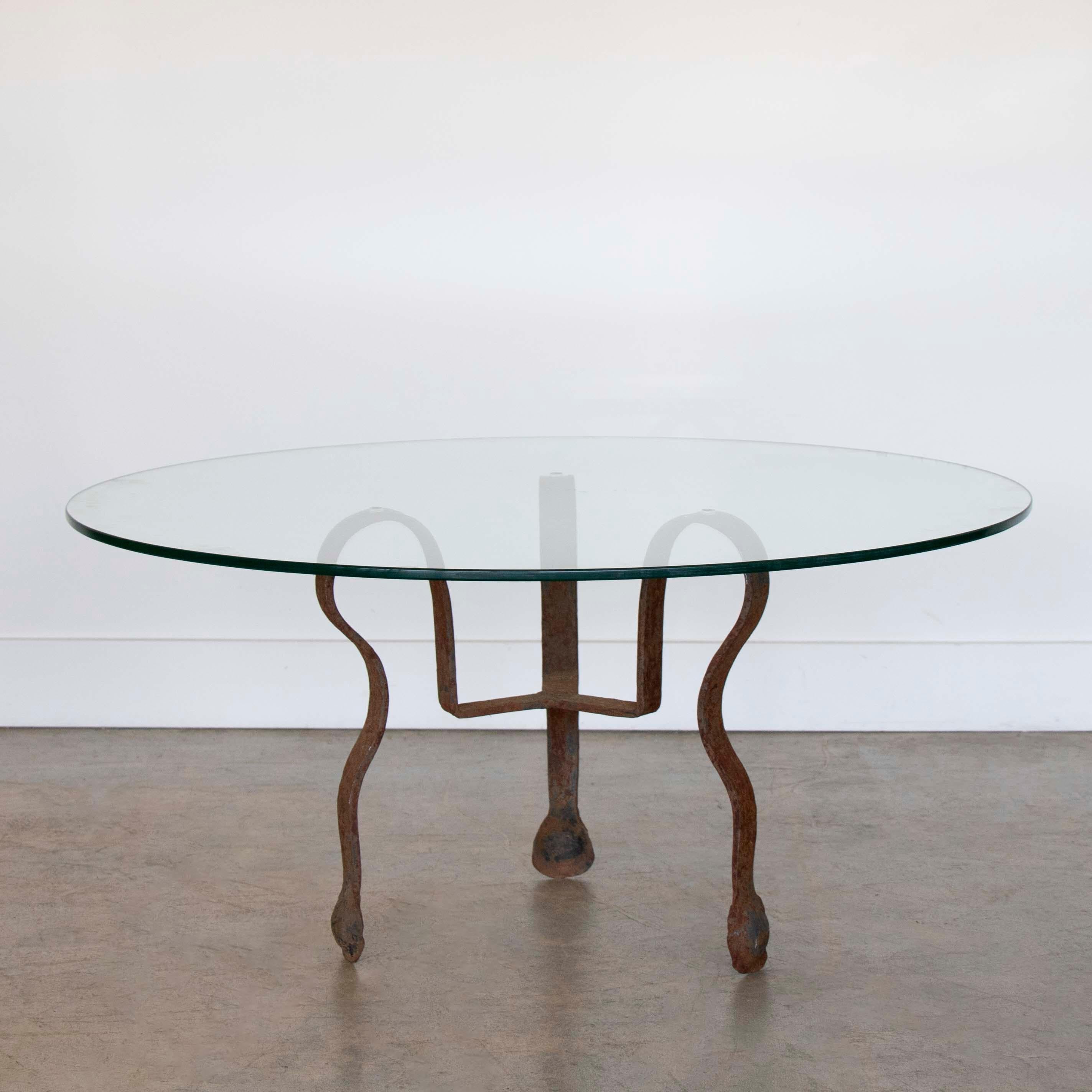 Beautiful glass and iron coffee table from Spain, 1920s.  Sculptural heavy iron base with 3 curved legs. Newly made circular glass top. Original iron finish shows nice age and patina with some rust. Unique statement piece. 