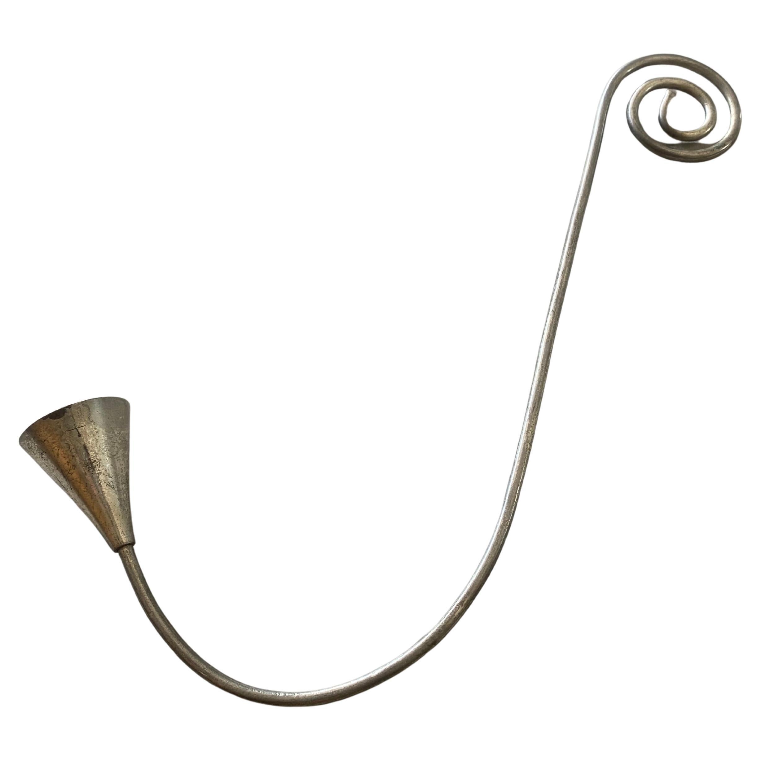 Skulpturaler Kerzenlöscher aus Metall mit einem (mitgelieferten) Aufhängehaken - funktional und ästhetisch ansprechend. Die langgestreckte, geschwungene Form vermittelt einen Hauch von Eleganz, während die abgenutzte Oberfläche und der