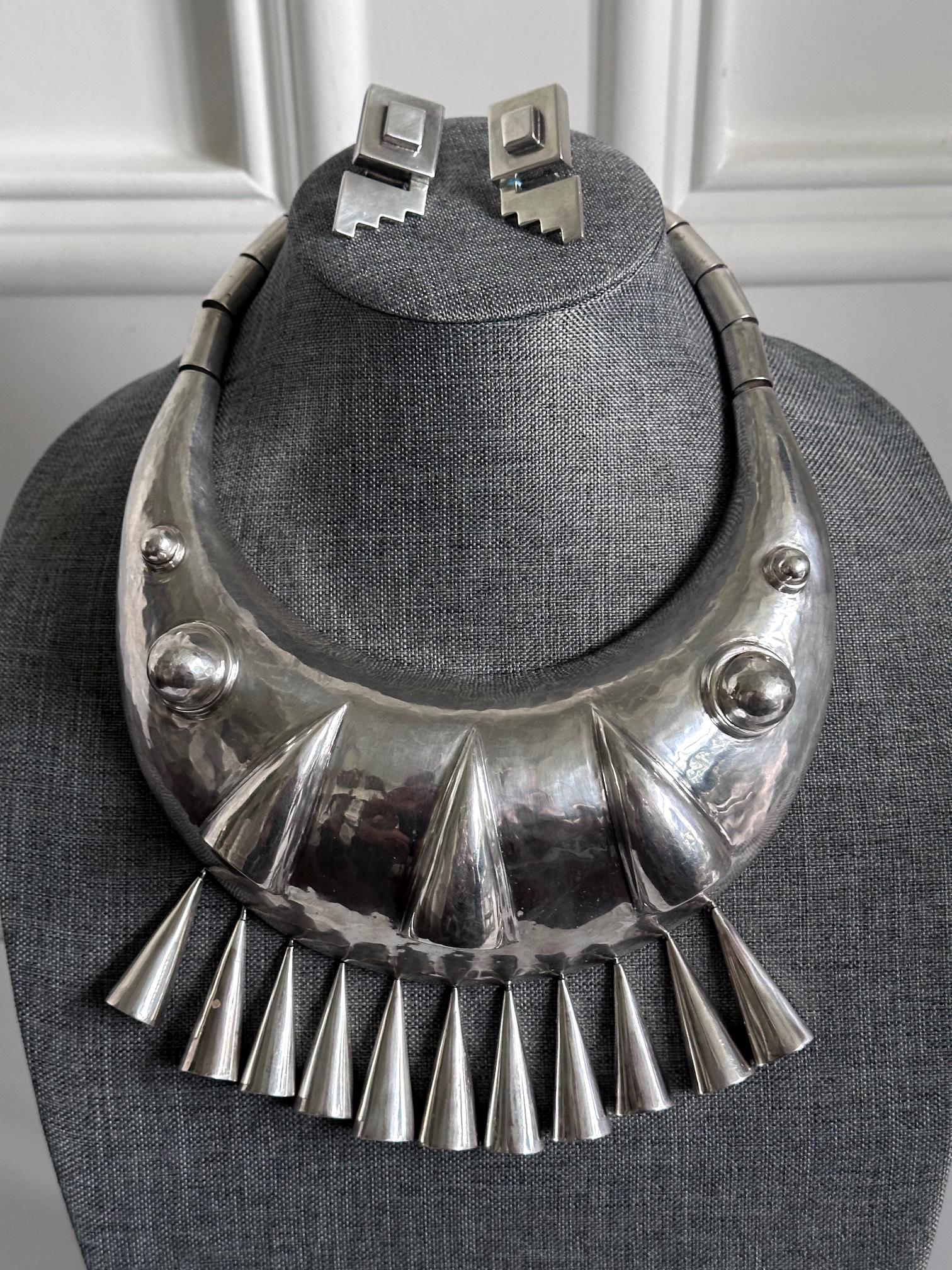 Conjunto de joyas de plata de ley de diseño atrevido de Graziella Laffi (1923-2009), Lima, Perú, hacia la década de 1970. El conjunto consta de un collar gargantilla muy escultural y un par de pendientes de forma geométrica inspirados en el motivo