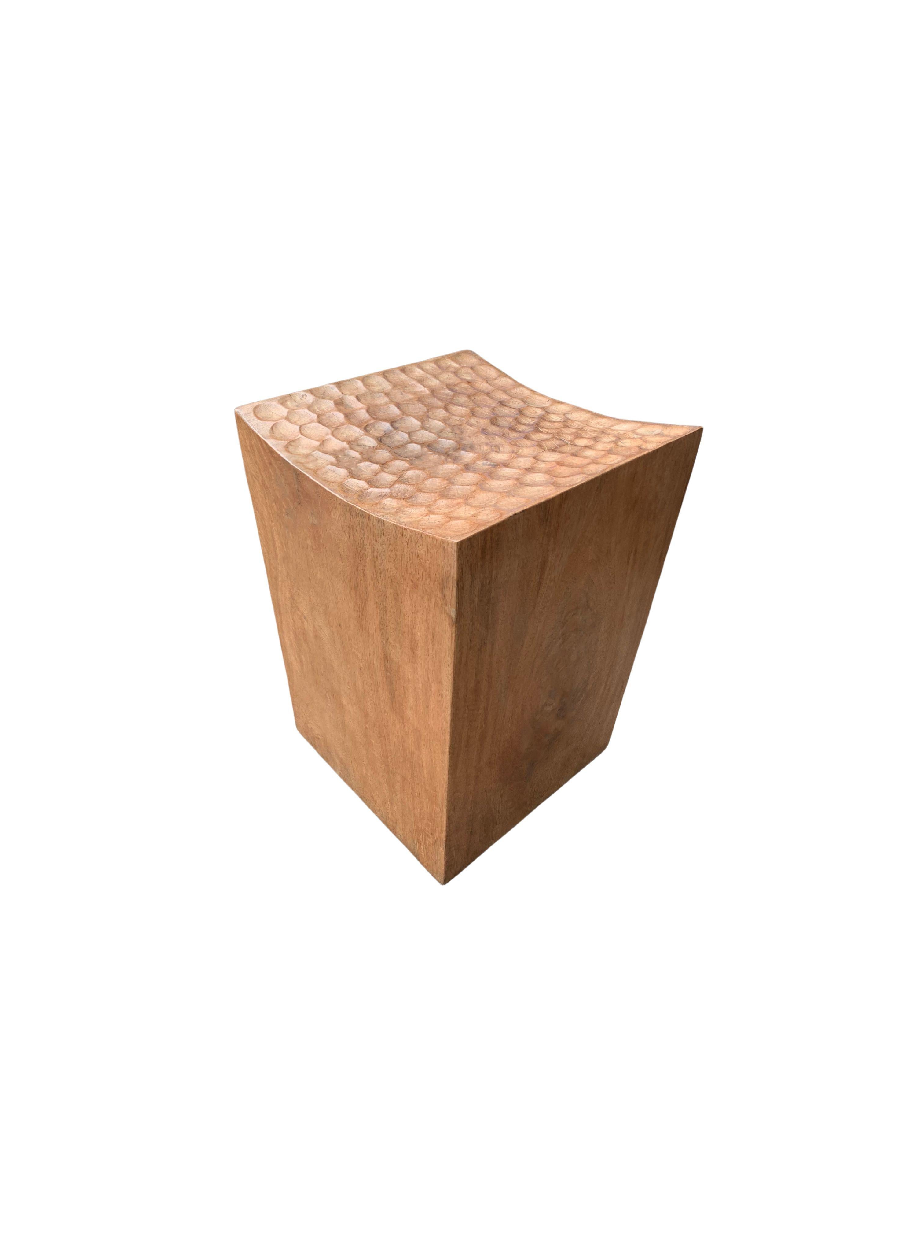 Ein wunderbar skulpturaler Hocker mit einer Mischung aus Holztexturen und -tönen. Dieser einzigartig skulpturale und vielseitige Stuhl wurde aus einem einzigen Block Mangoholz gefertigt und hat eine glatte Maserung. Sorgfältig geschnitzt,