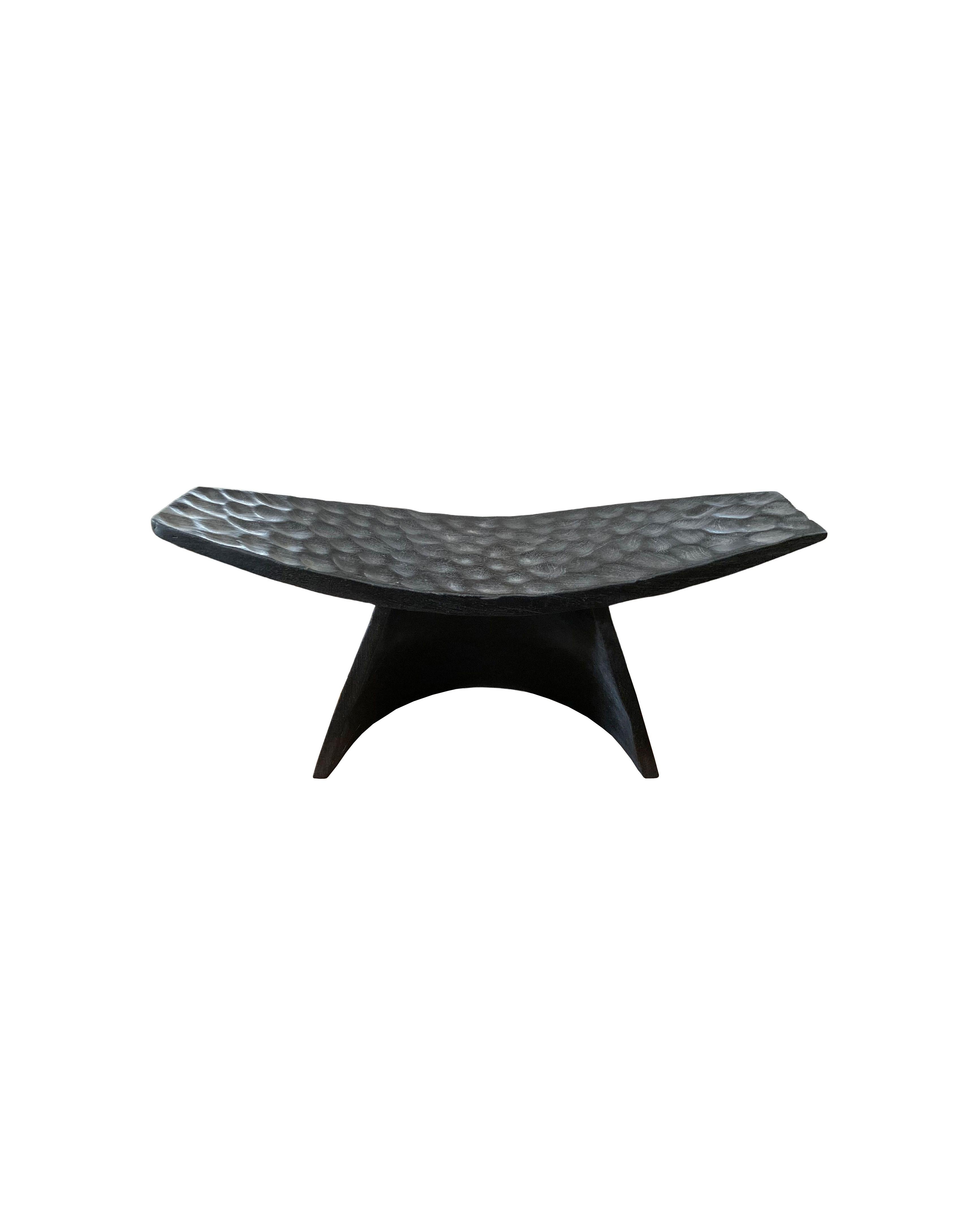 Un taburete maravillosamente escultural con asiento curvado y detalles tallados a mano. Su rico pigmento negro se consiguió quemando la madera tres veces. El pigmento neutro del taburete y su sutil textura de madera lo hacen perfecto para cualquier