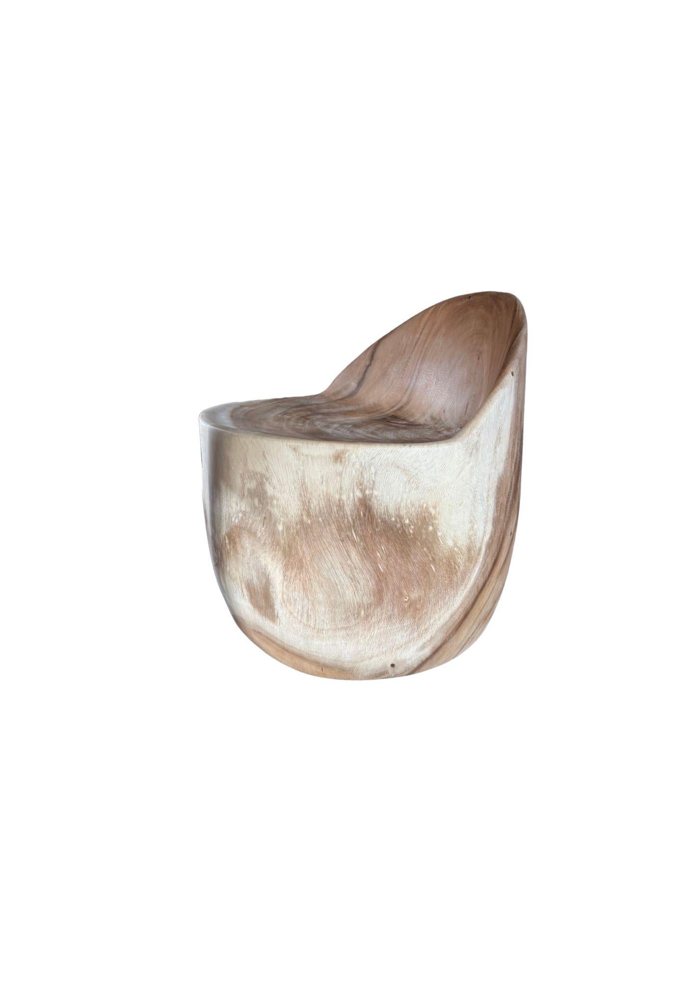 Tallada a mano a partir de un único bloque de madera maciza de suar, esta silla escultural muestra la belleza orgánica y los fluidos patrones de veteado exclusivos de la especie. Su forma suave y redondeada y su asiento suavemente curvado crean un
