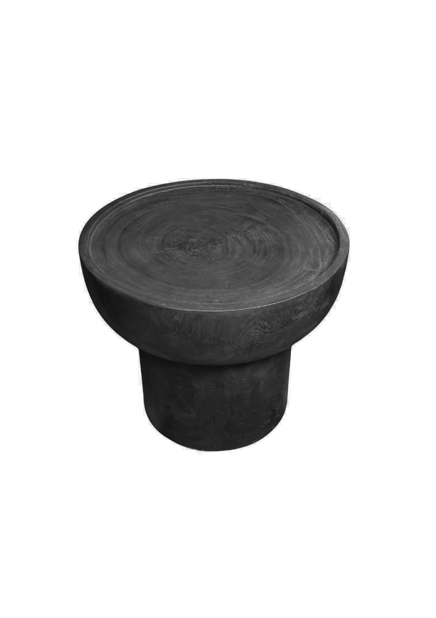 Cette table d'appoint en bois de Suar présente une finition noire brûlée spectaculaire, créée par un processus de carbonisation en plusieurs étapes qui met en valeur le grain naturel et la profondeur du bois. Le résultat est une riche surface noire