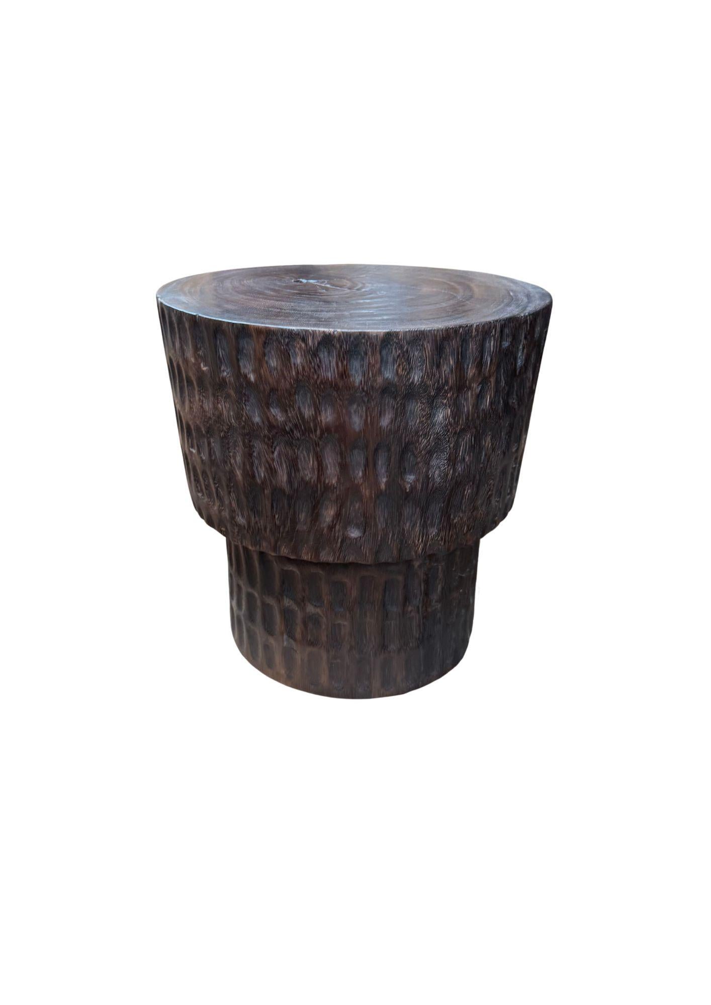 Questo tavolino scultoreo presenta una ricca finitura marrone scuro, ottenuta grazie a un processo di combustione in più fasi che esalta le venature naturali e la profondità del legno. La sua silhouette audace è completata da dettagli