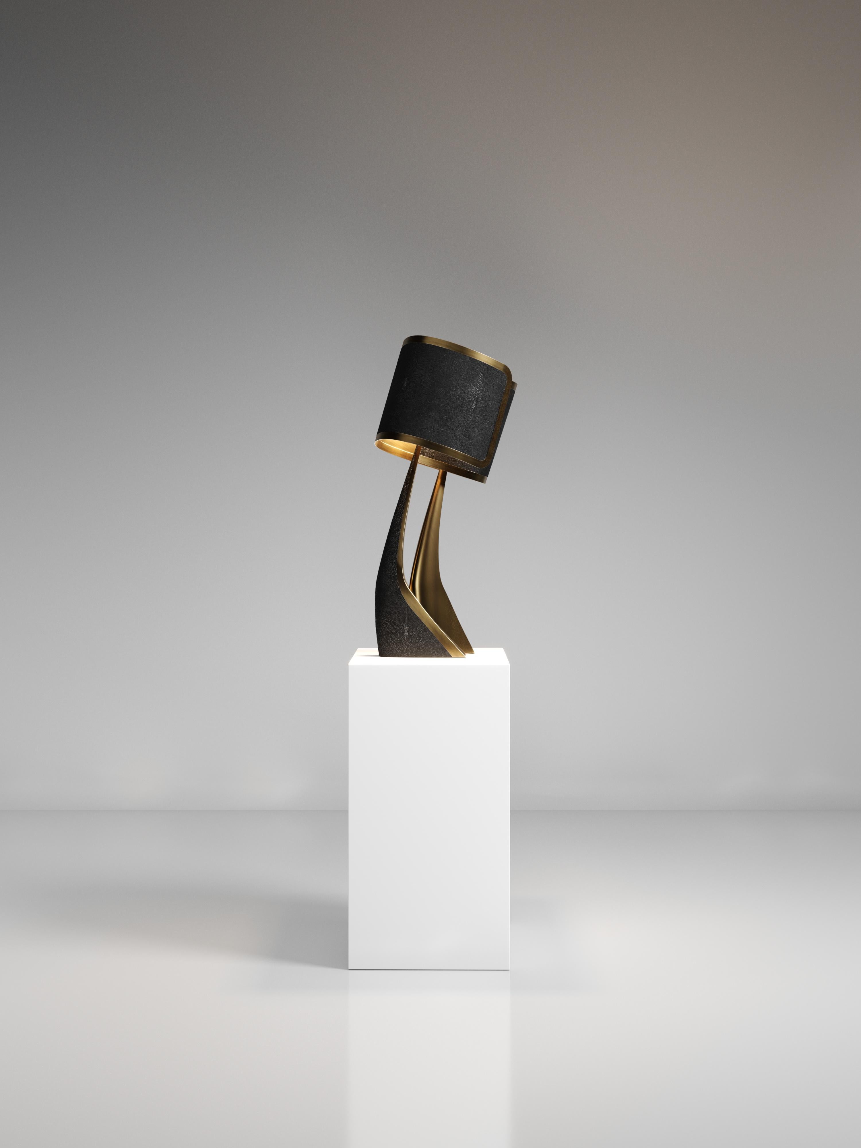 The Chital III Table Lamp by Kifu Paris is a sleek and sculptural piece, inlaid in a mixture of bronze-patina brass and cream shagreen. The chiseled legs, which are an iconic shape within the KIFU PARIS universe, morph into the solid shades that