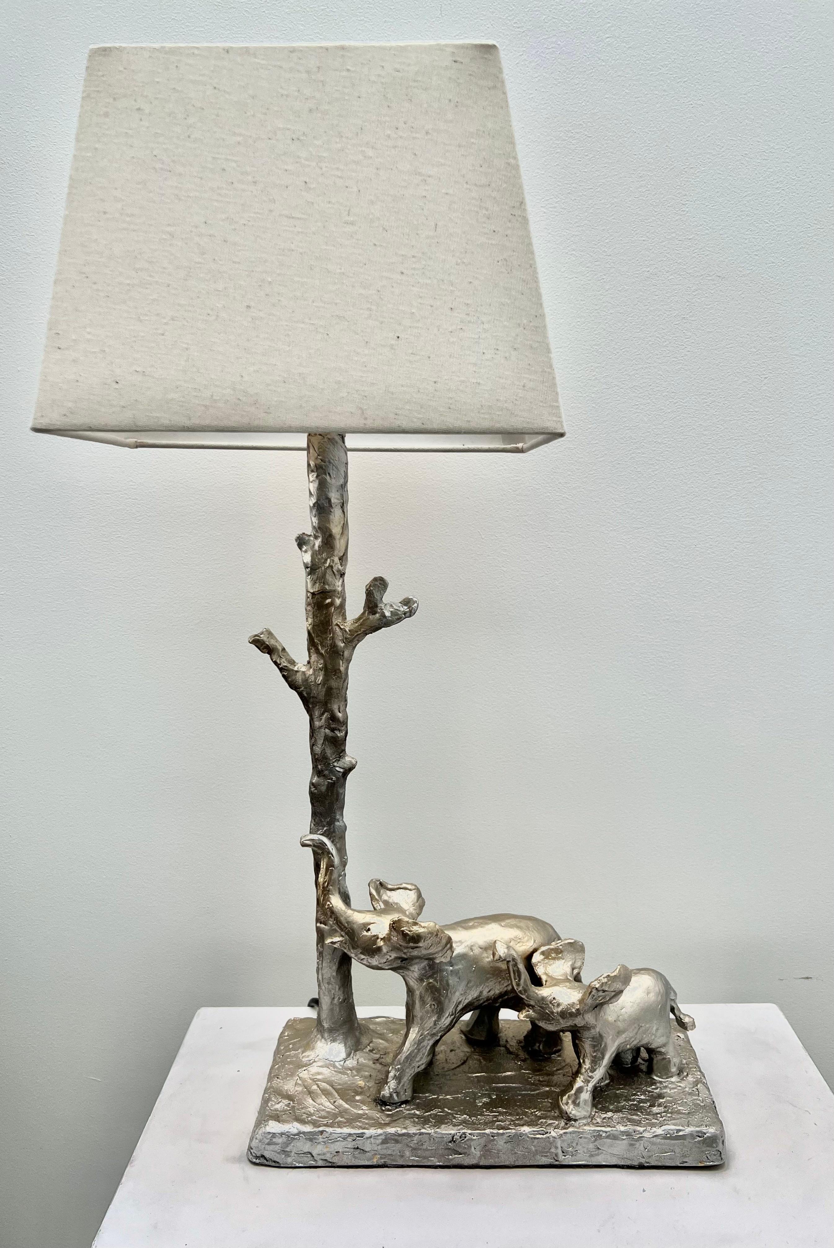 A  lámpara de mesa escultórica de  madre y cría de elefante paseando alegremente  con los troncos hacia arriba . Una obra de arte funcional,  Hecho a mano, moldeado y fundido en resina. 
Todas las piezas de la lámpara están fabricadas