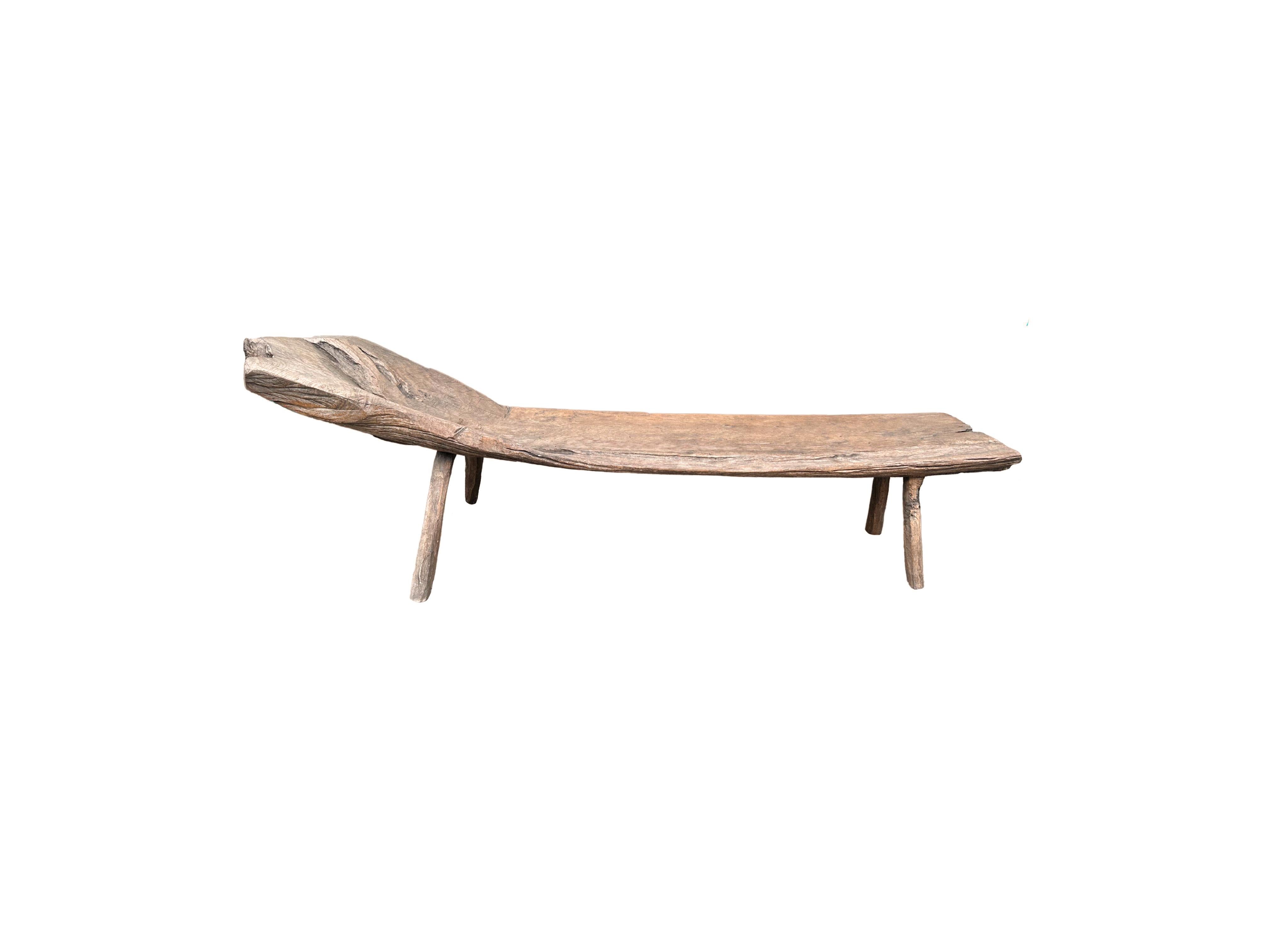 This hand-carved teak wood bench originates from the Island of Madura, off the coast of Northeastern Java. It features a long slender form with angular legs. A wonderful sculptural object with wood textures and shades. The seat was carved from a