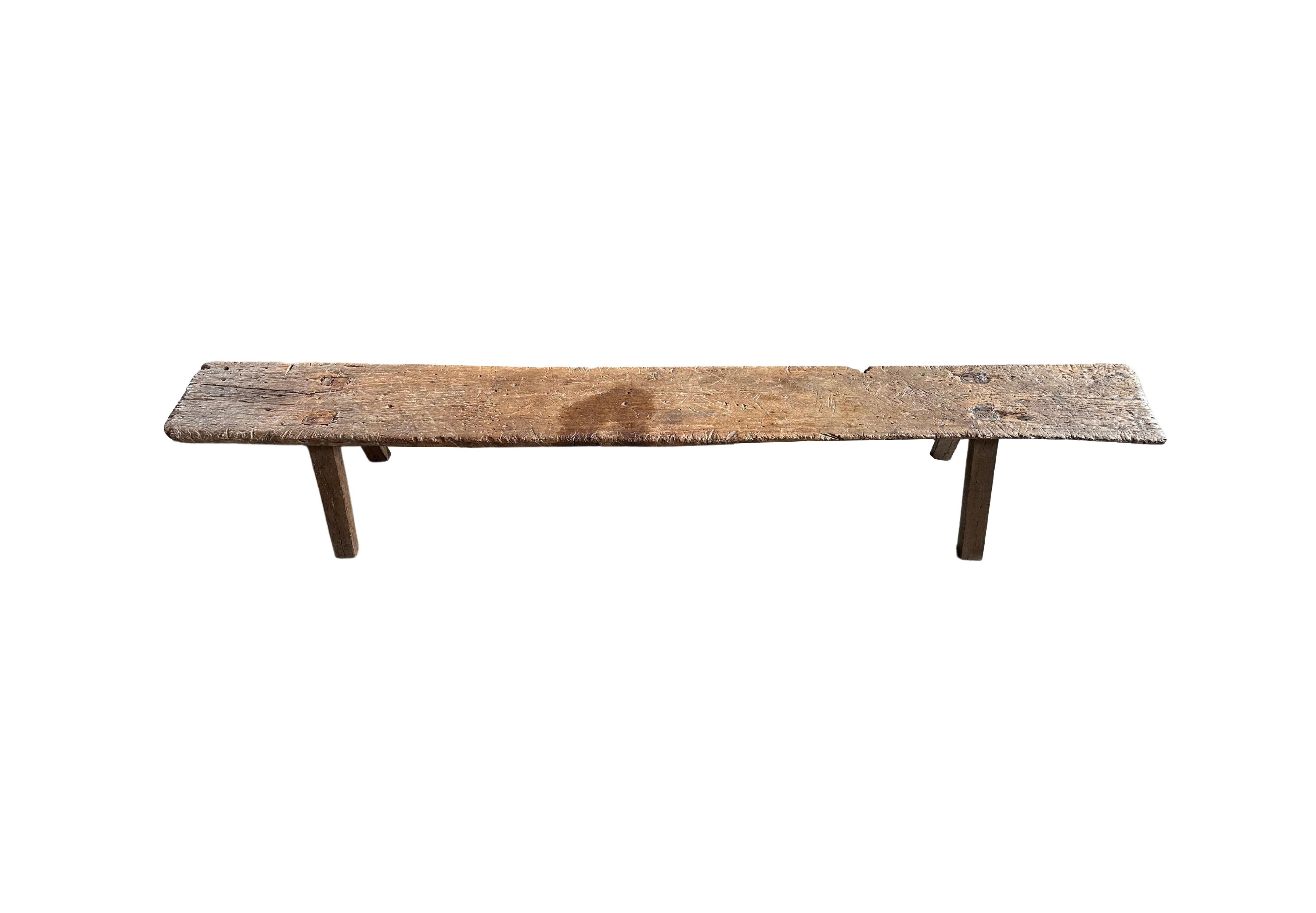 This hand-carved teak wood bench originates from the Island of Madura, off the coast of Northeastern Java. It features a long slender form with angular legs. A wonderful sculptural object with wood textures and shades. The seat was carved from a