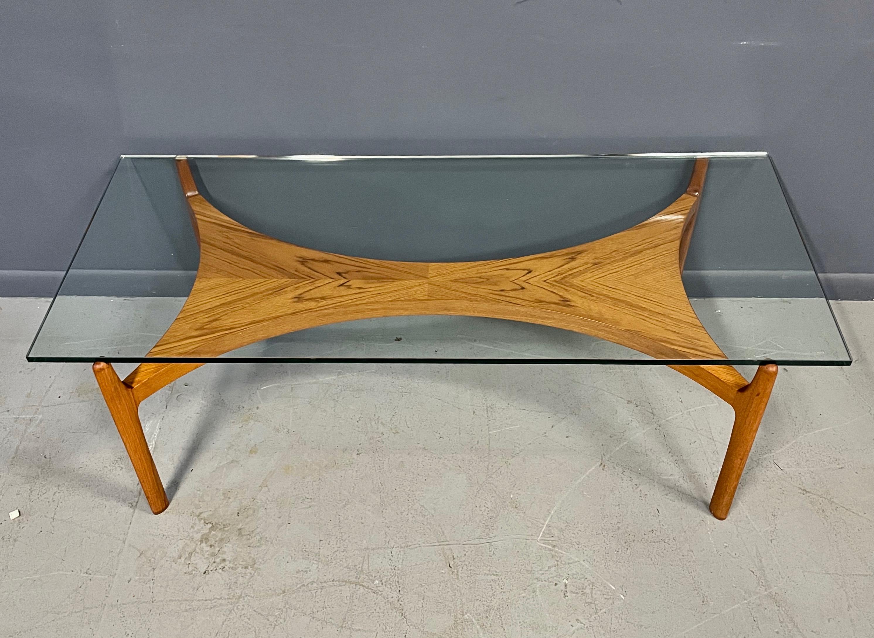 A Scandinavian Modern vintage coffee table designed by Sven Ellekaer 1960s, which was made of solid teak and veneered teak. The sculptural teak base is topped with an original clear glass plate.