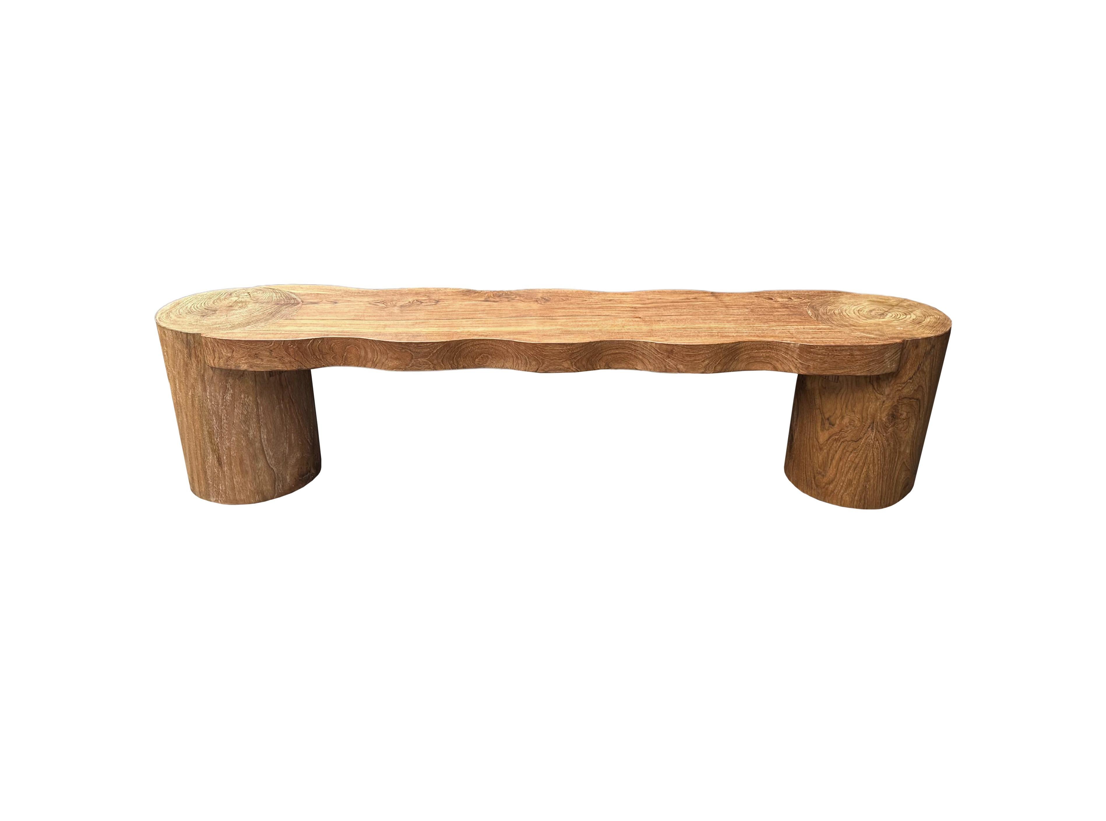 This bench was sculpted from solid teak wood with an elegant mix of contours. The wood used to create this bench is reclaimed, sourced from old pillars of traditional Java Houses, from the island of Java, Indonesia. It features a natural finish with