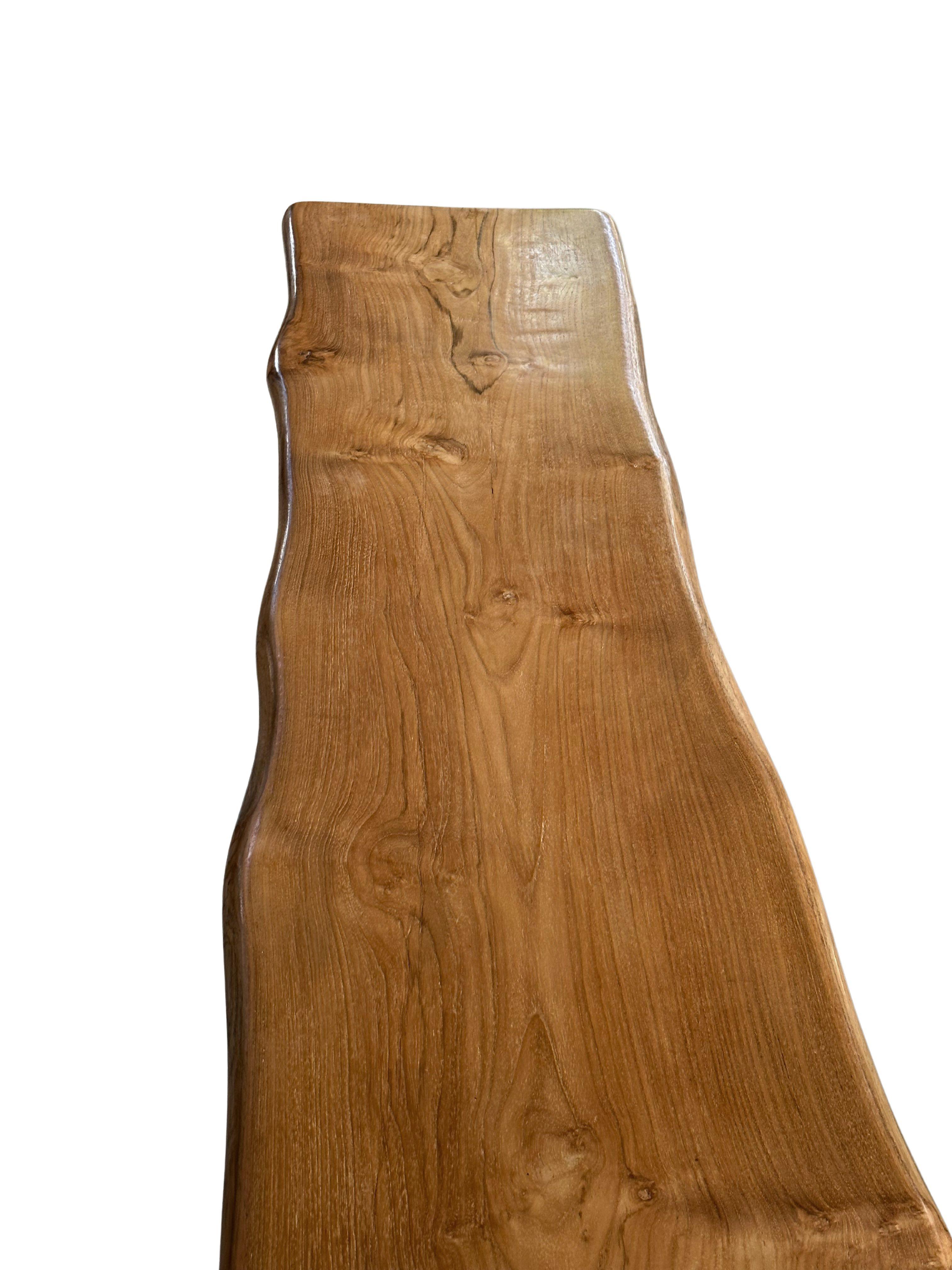 This teak wood bench is a masterpiece of natural elegance, showcasing the stunning textures of the rich, golden-brown teak grain. Its smooth, polished surface highlights the wood’s inherent beauty, with intricate variations in color and pattern that