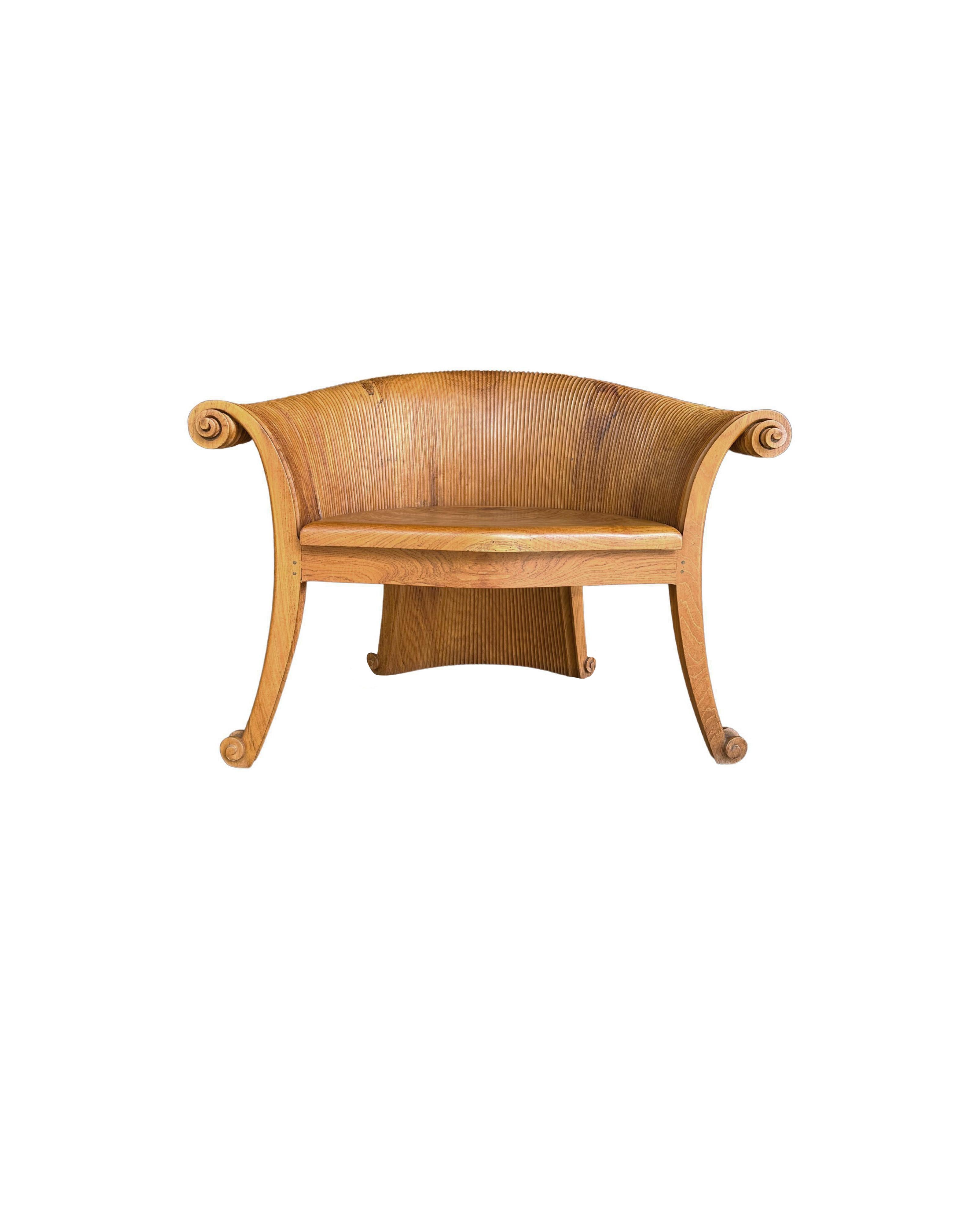 A wonderfully sculptural teak wood chair featuring intricately carved curves and ribbed detailing. Resembling a curved lotus leaf it features a strong organic form. The mix of wood textures and shades adds to its charm. A unique piece of
