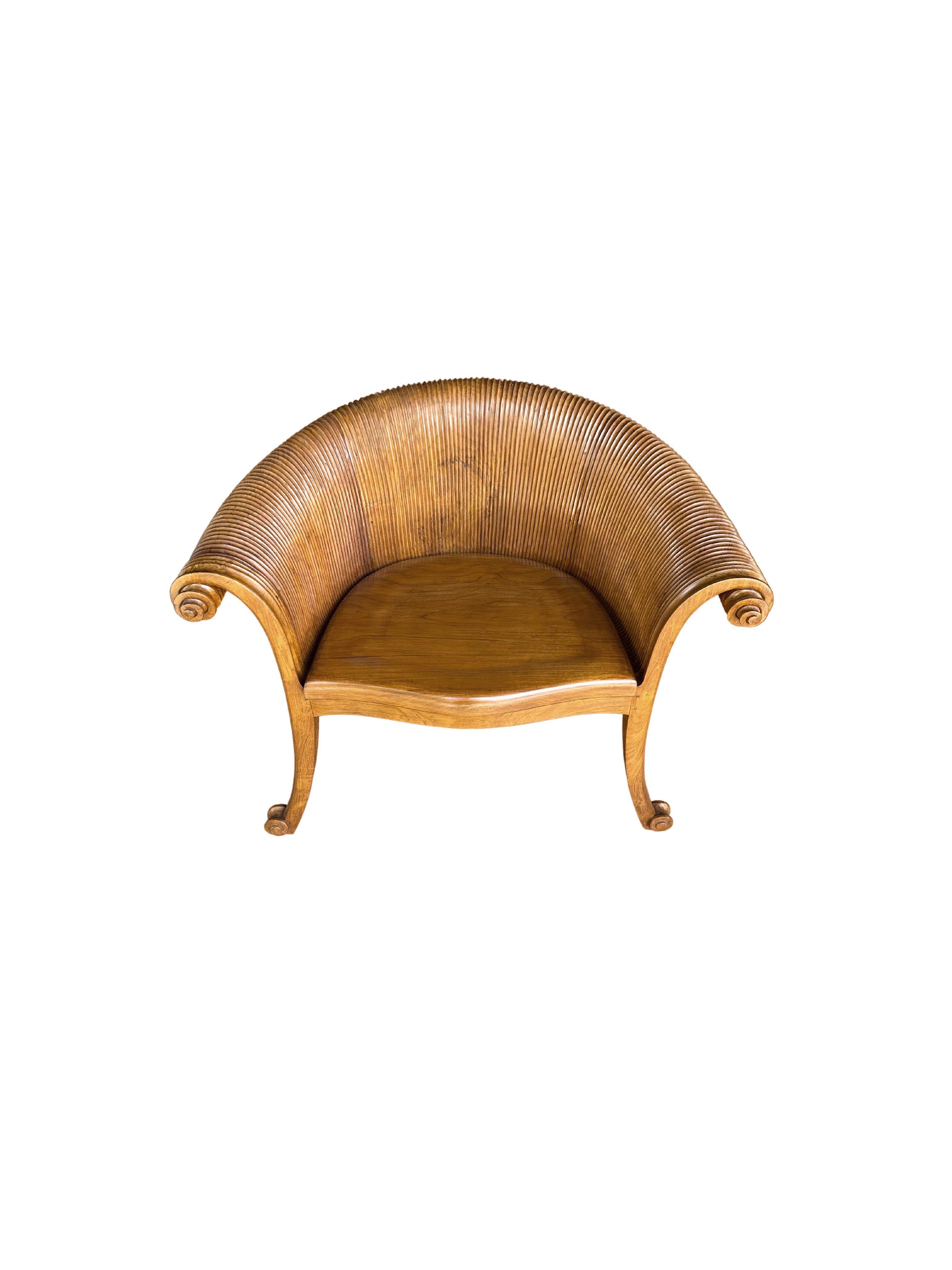A wonderfully sculptural teak wood chair featuring intricately carved curves and ribbed detailing. Resembling a curved lotus leaf it features a strong organic form. The mix of wood textures and shades adds to its charm. A unique piece of