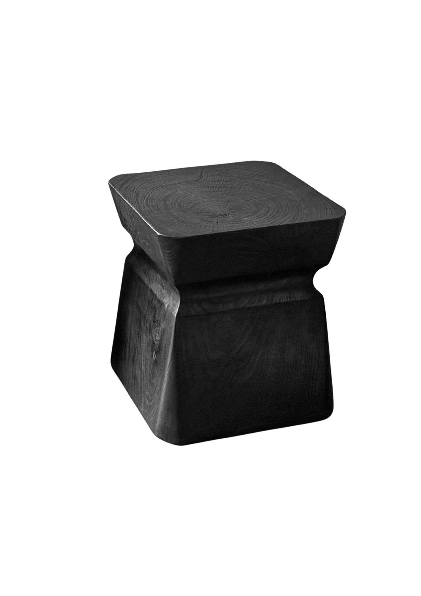 Crafted from a single, solid block of premium teak wood, this sculptural side table showcases the raw beauty and strength of its material. Its surface reveals stunning natural wood textures and organic grain patterns, each highlighted by a dramatic