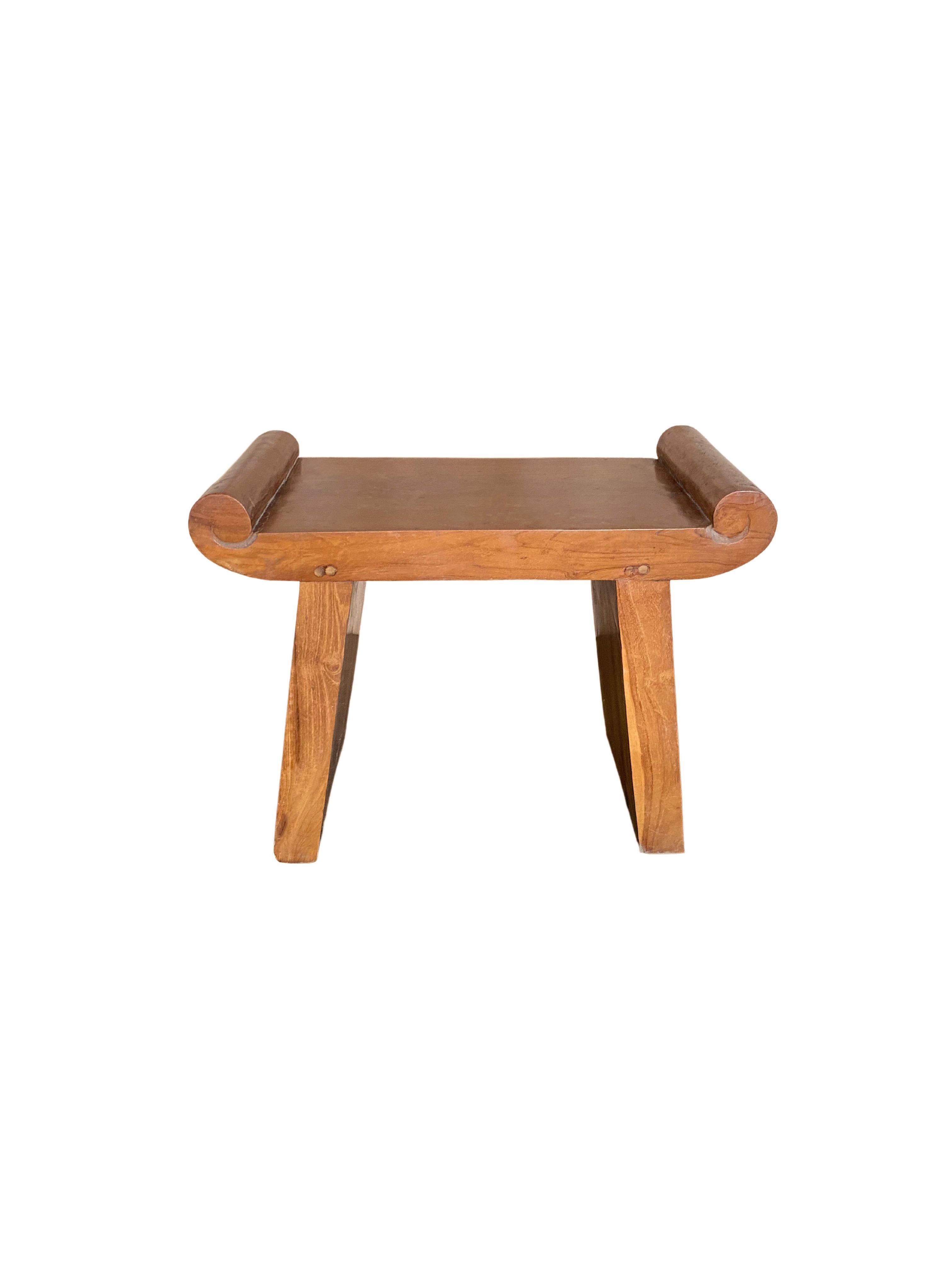 A wonderfully sculptural teak wood stool. The seats subtle wood carved detailing gives it the impression that is has curled ends. The contrast of the curved detailing with the stools angular legs adds to its charm. Its subtle wood textures and