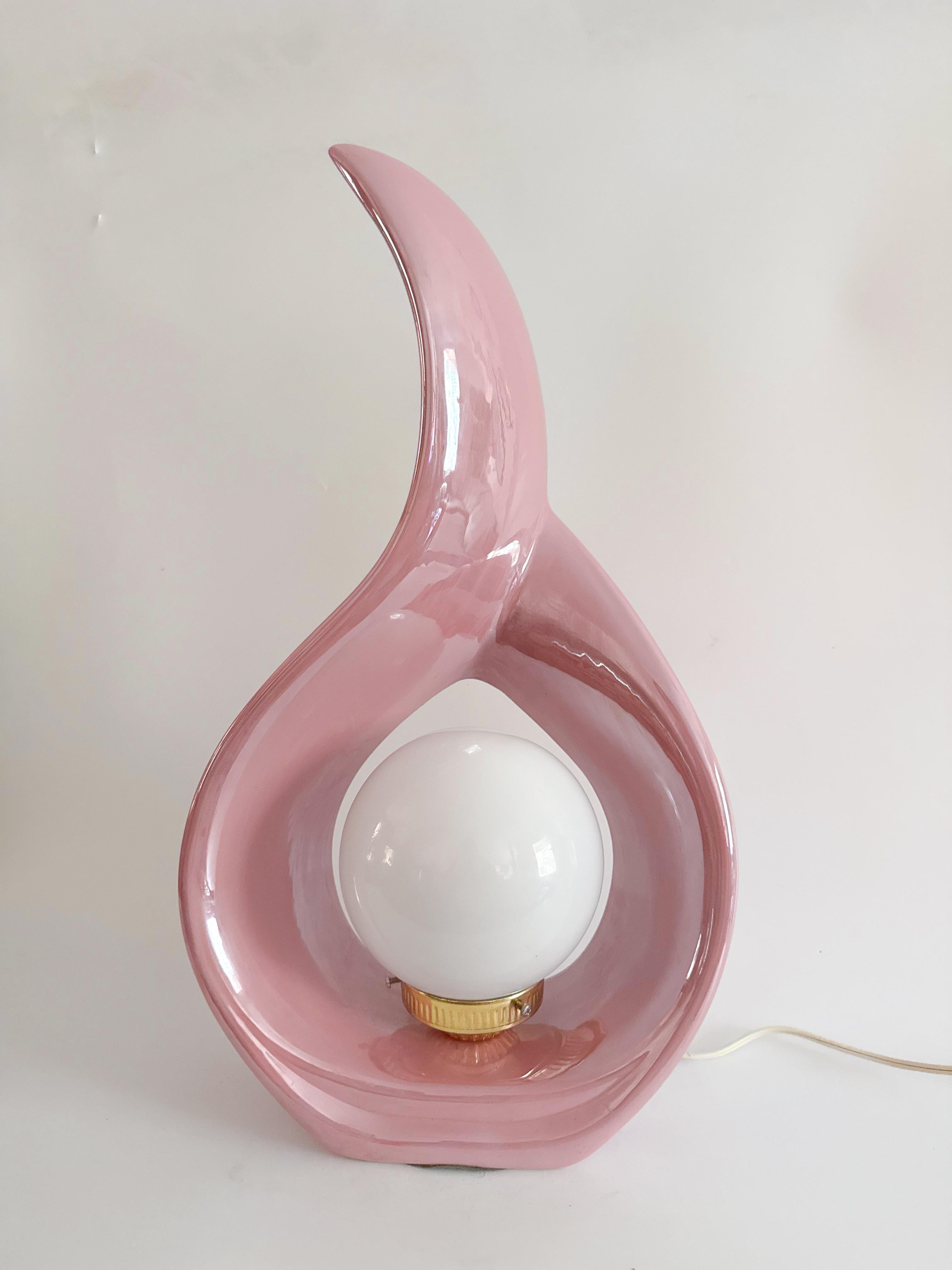 Brillante, dimensional y llena de movimiento, esta escultural lámpara de cerámica de los años 80 es un raro hallazgo en un impresionante esmalte rosa iridiscente. Su silueta llameante fluye hacia arriba en una grácil curva, acunando en su centro un