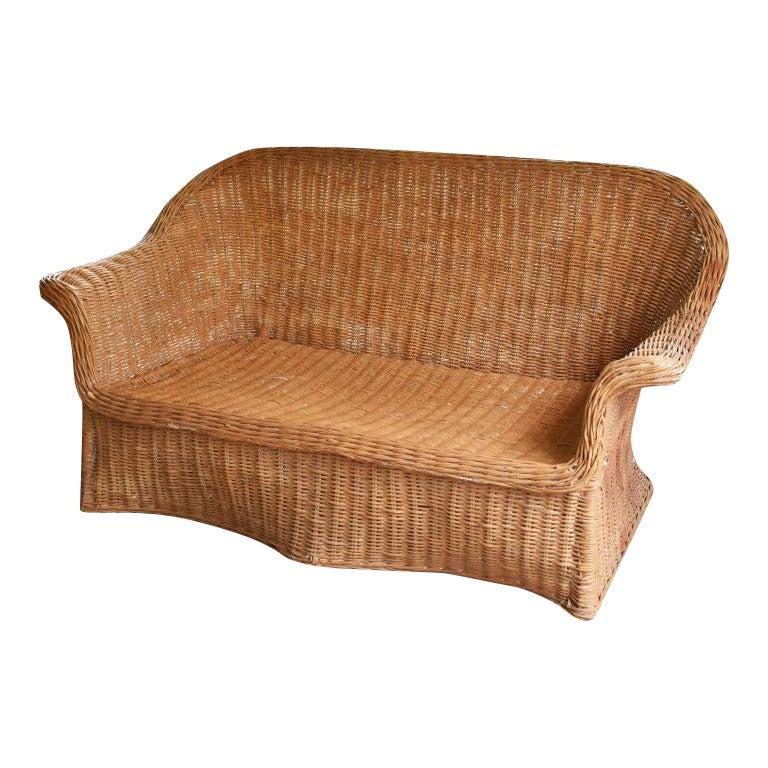 Lovely sculptural Hollywood Regency Trompe L'Oeil draped wicker weave rattan ghost sofa with arms. A great piece loveseat which is perfect for two. This sought after draped piece is a cult favorite amongst design aficionados. The piece is woven of