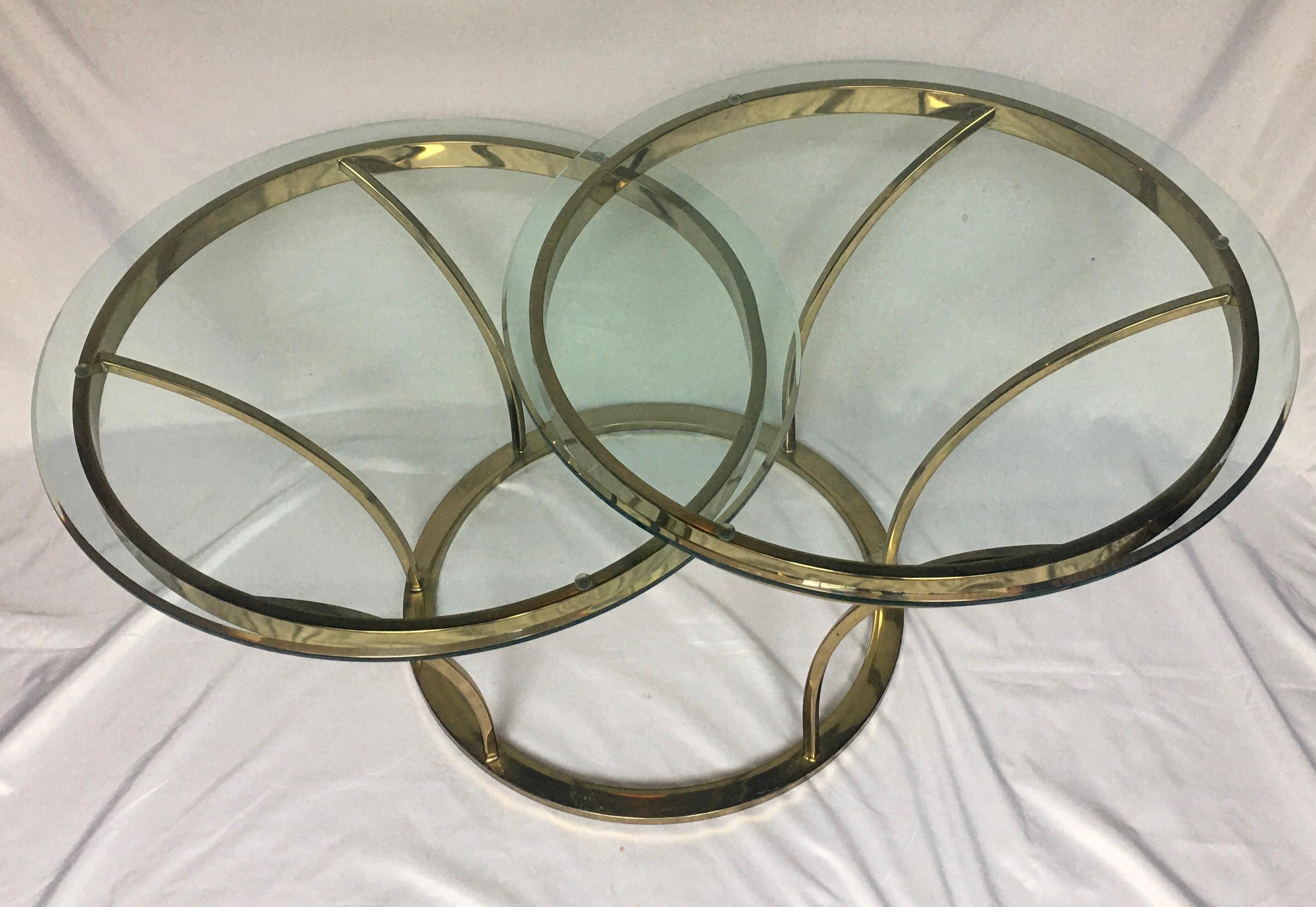 Sculptural 1970s brass-plated metal and glass center coffee or cocktail table. Sculptural curved design features two beveled round glass tops, tiered at different heights for a unique asymmetrical look. Style of Milo Baughman.

Top tier one: 25 W,