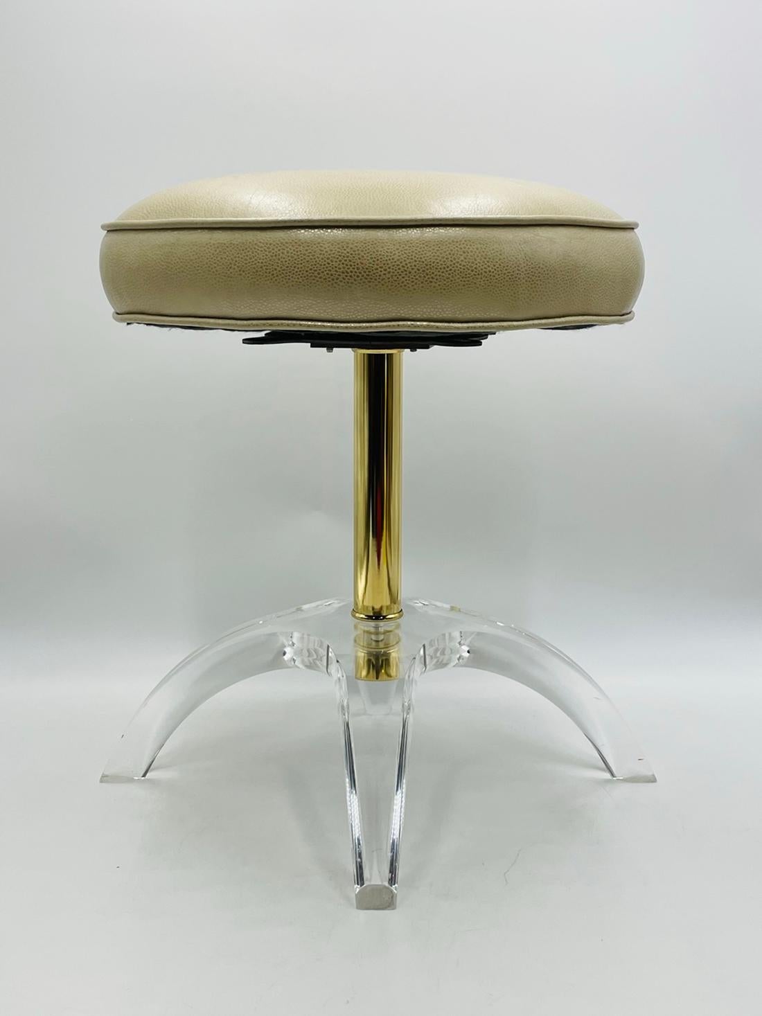 Stunning vanity stool designed and manufactured in the 1960s by Charles Hollis Jones.

The stool has a sculptural Lucite base with a brass stem/rod and a swivel seat upholstered in a cream color vinyl seat.

The stool is in very good original