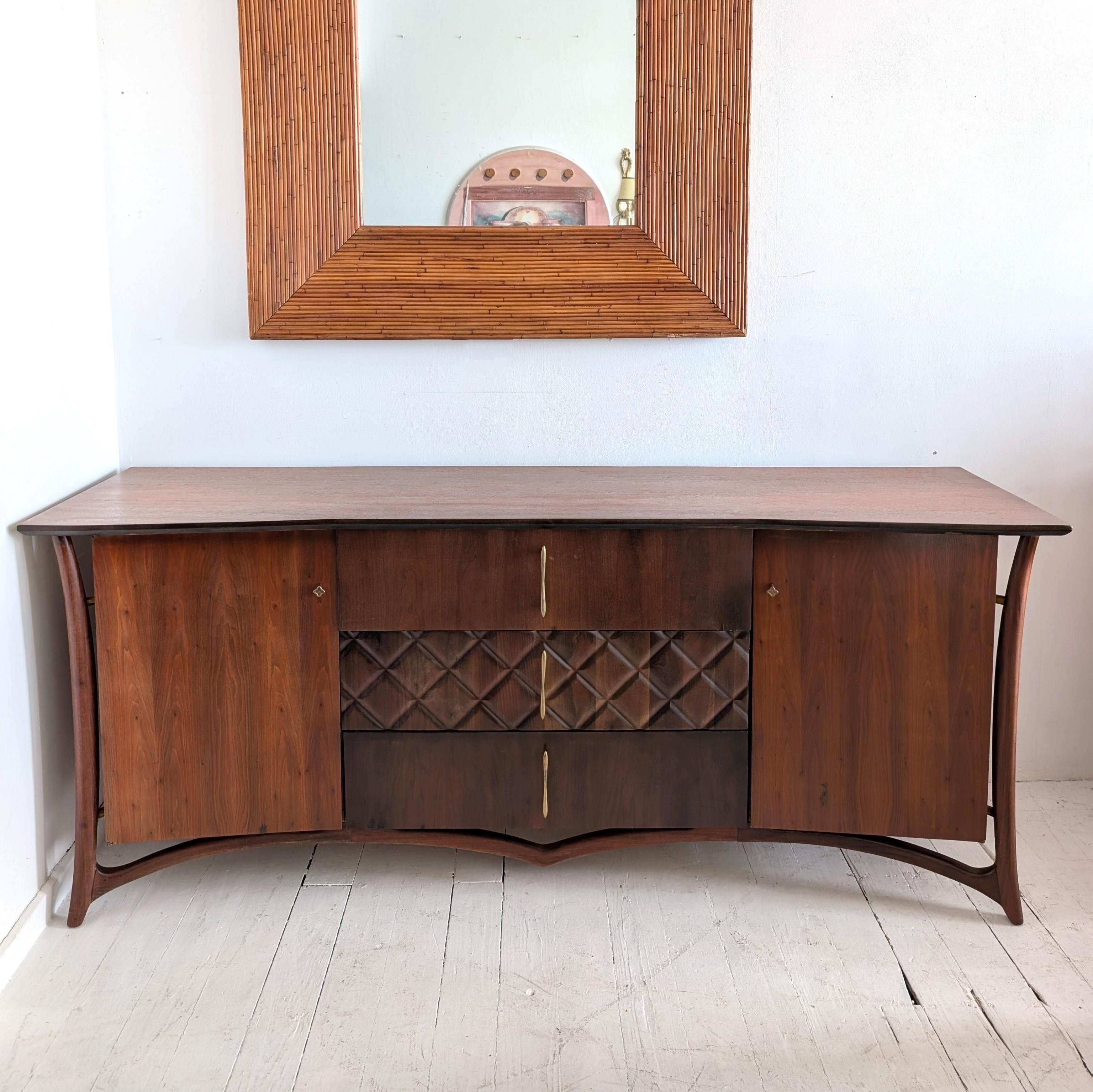 Spectacular walnut sideboard by Piet Hein, Denmark 1960s is a rare beast. Striking exoskeleton frame- with brass details at the ends- around the body; 'bowtie' shaped top; carved quilted central drawer; sculptural gilt metal handles.
Three large