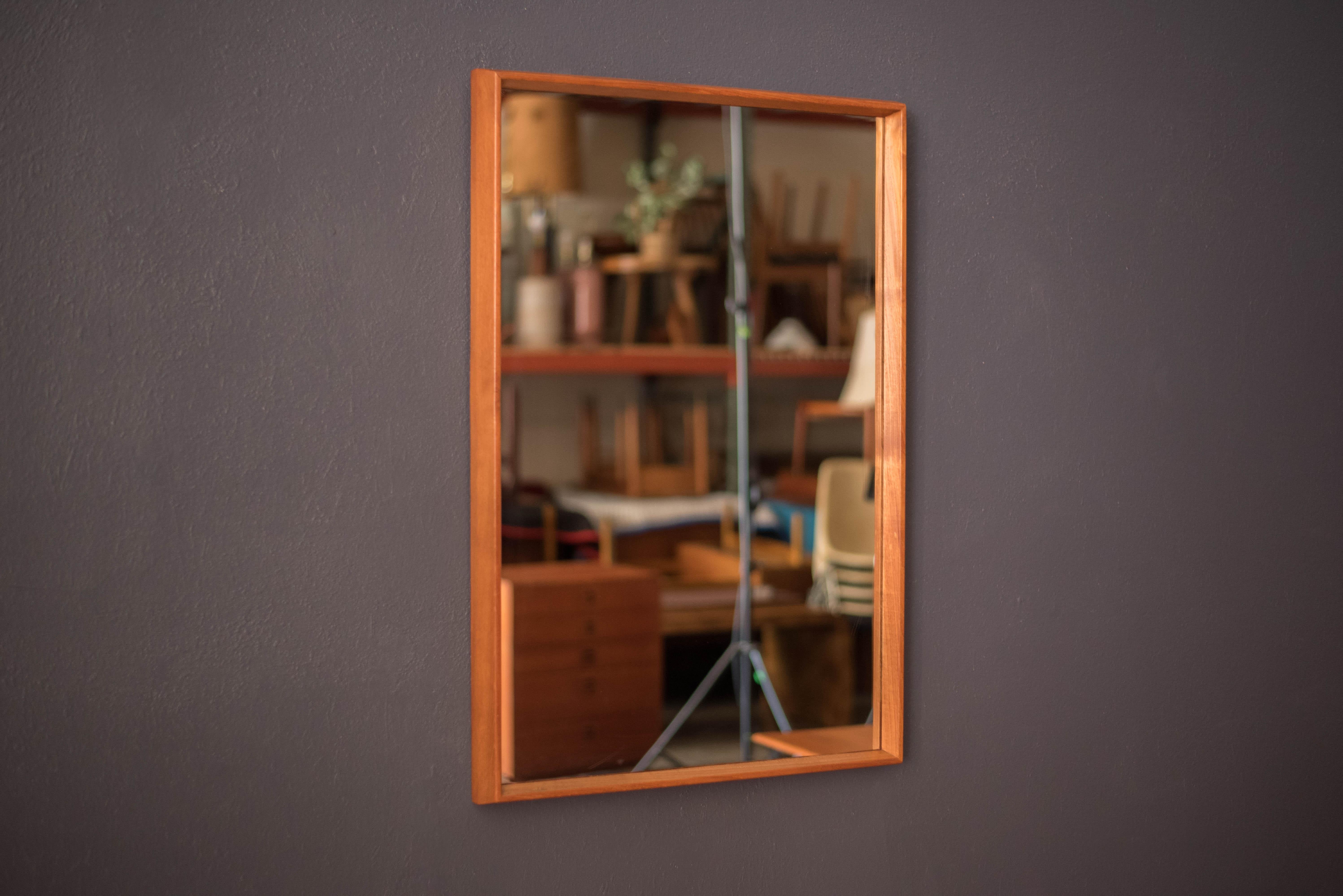 Mid-Century Modern accent hanging wall mirror in teak circa 1960s. This versatile piece displays a contoured natural wood frame in a rectangular mid-length shape. Fits perfectly in an entryway, bedroom or hallway space and can be mounted wide or