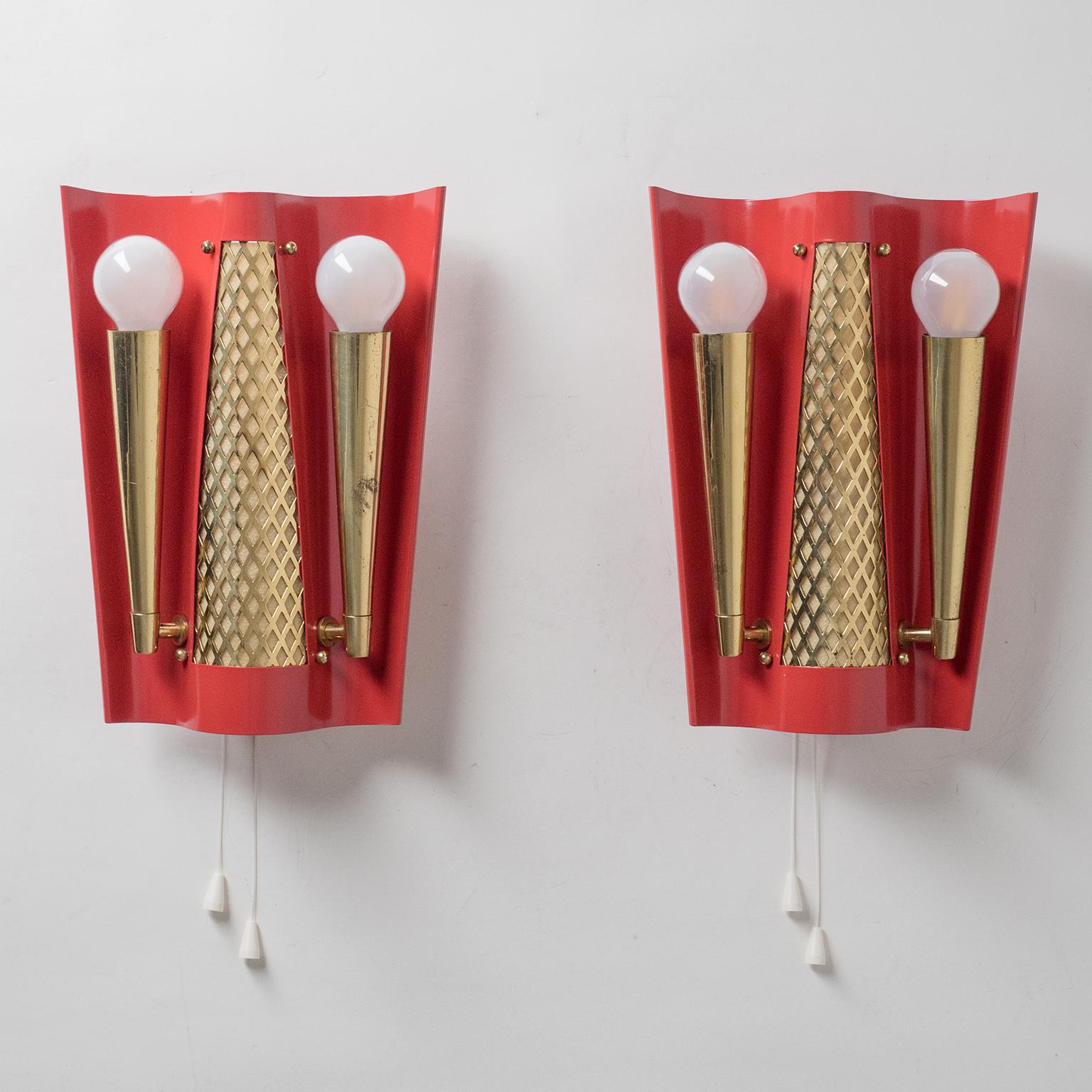 Rare pair of 'theatrical' wall lights, circa 1950. Curved steel backplate enameled in red with brass decorative elements and socket covers. Each unit has three original brass E14 sockets - two in the front and one on the back, which can be