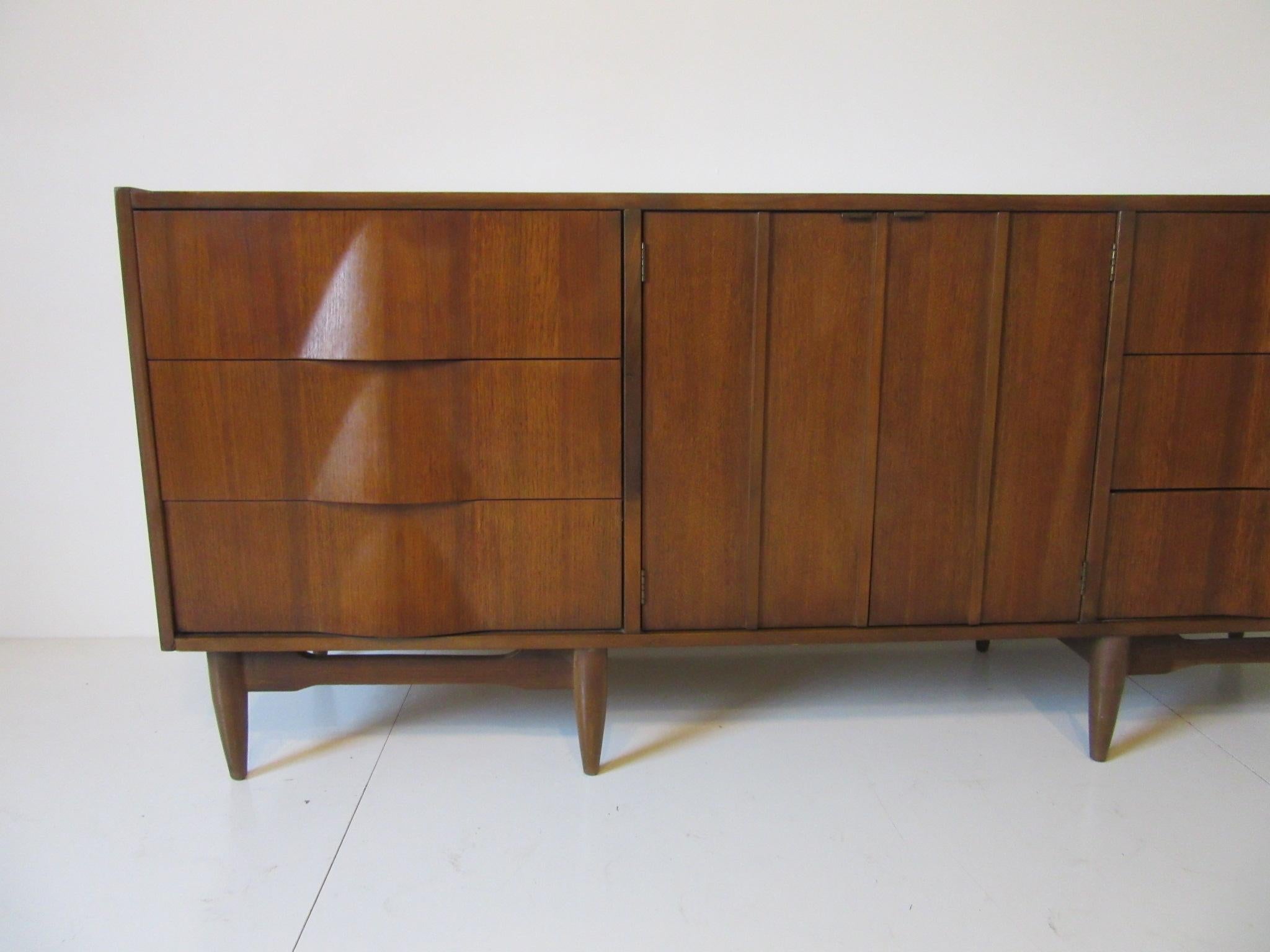 A well grained midcentury walnut dresser chest with six side drawers and two middle doors reveling three additional drawers. The sculptural design incorporates the pulls to each outer drawer front giving this piece an organic vibe in the manner of