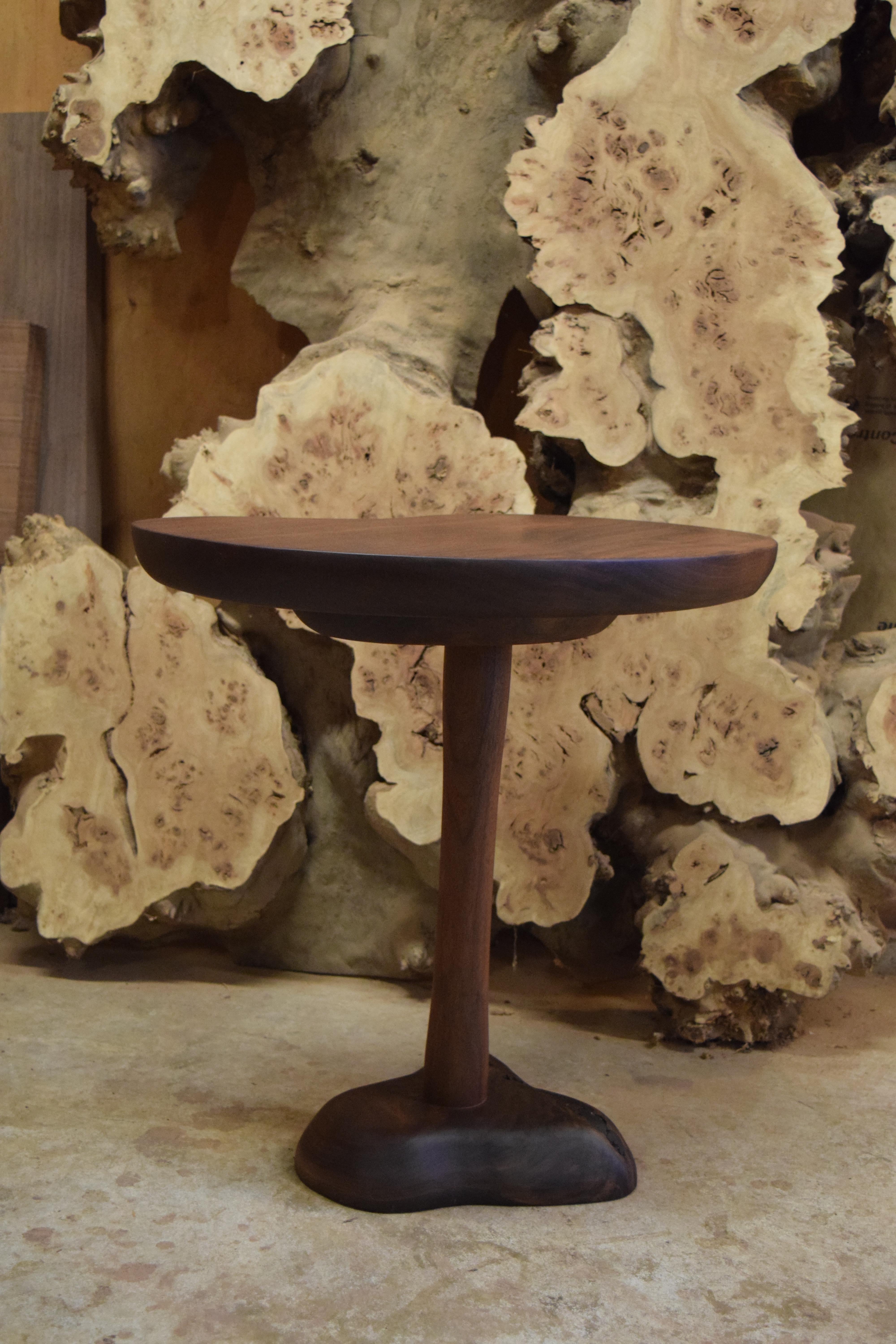 Il s'agit d'une table d'appoint sculpturale, fabriquée à la main, en noyer massif, avec une base sculptée et un plateau en forme de rein. La partie supérieure présente des courbes douces et un arrondi prononcé sur la partie inférieure. Sous le