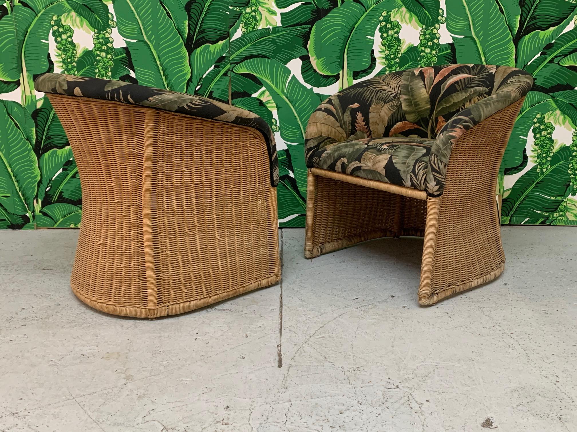 Pair of wicker club chairs feature sculptural design and tropical palm leaf print upholstery. Good vintage condition with minor imperfections consistent with age. Price is for the pair. 
Measures: Seat height is 19