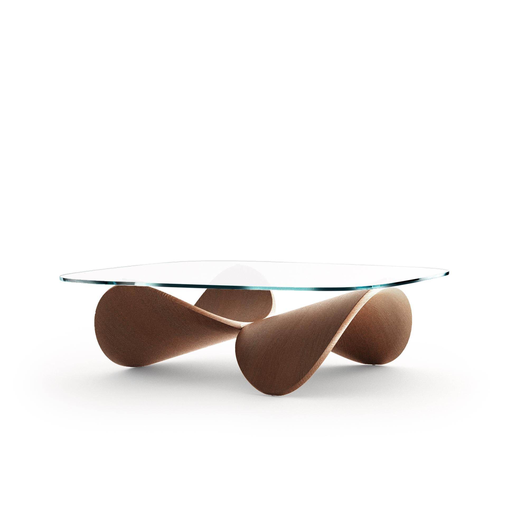 A coffee table that is both furniture and sculpture designed for authentic living spaces. Two identical wooden shells are arranged together in a reversed posture and are joined to create a sculptural structure for the glass top. 
The table was named