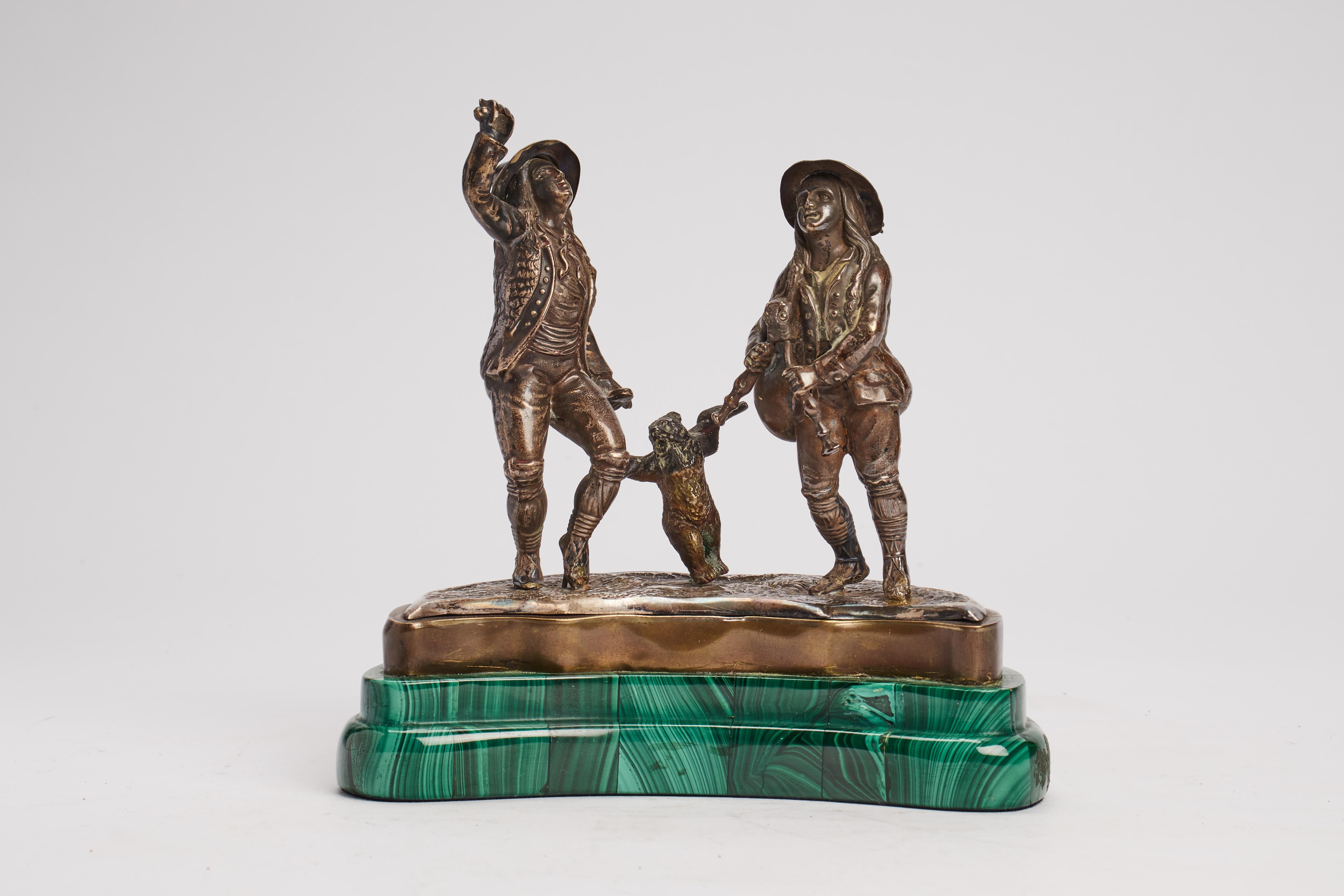 Silver sculpture depicting a piper, a dancer and a small dancing bear in the centre. Malachite base in the shape of a crescent moon Russia, around 1880.