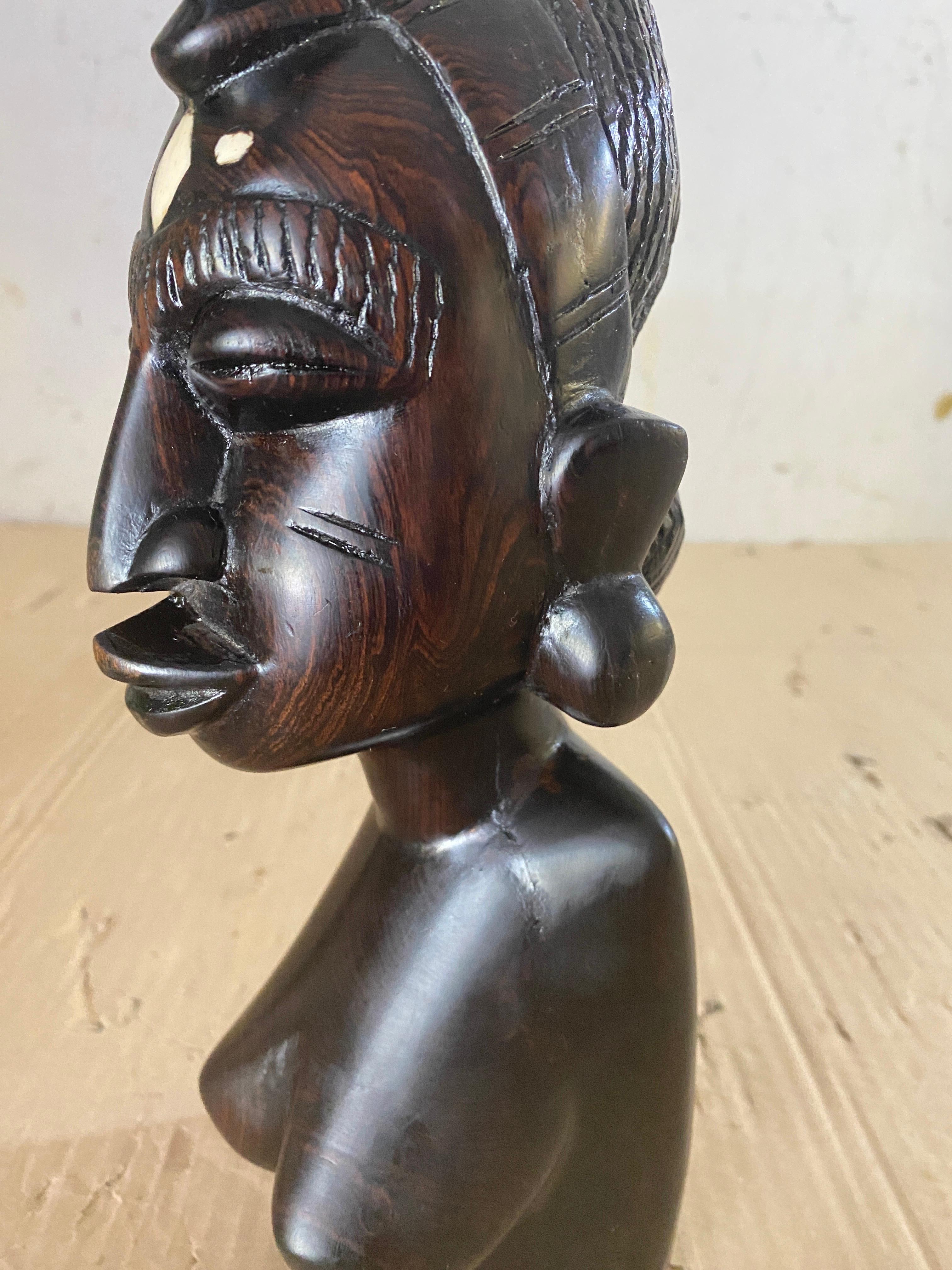 This sculpture is a bust of a woman, with it's traditional air cut. This is in wood, in a black color, and has been made in africa in the 20th Century.
