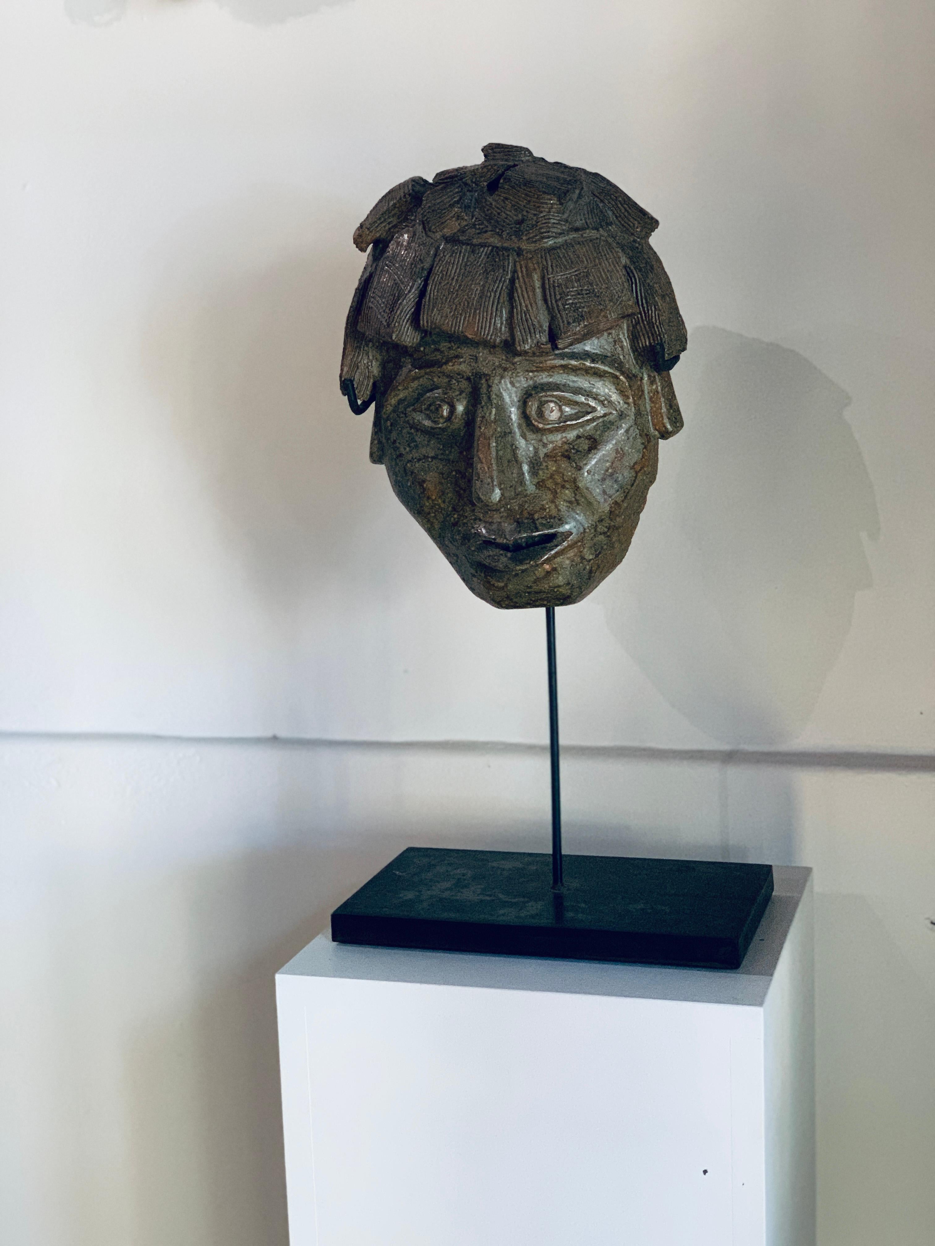 Masque en terre cuite avec une glaçure nuancée dans des tons de terre, allant du vert au brun.

Le modelage d'une grande finesse révèle une véritable maîtrise technique : des volumes expressifs, des détails délicatement incisés, une présence à la