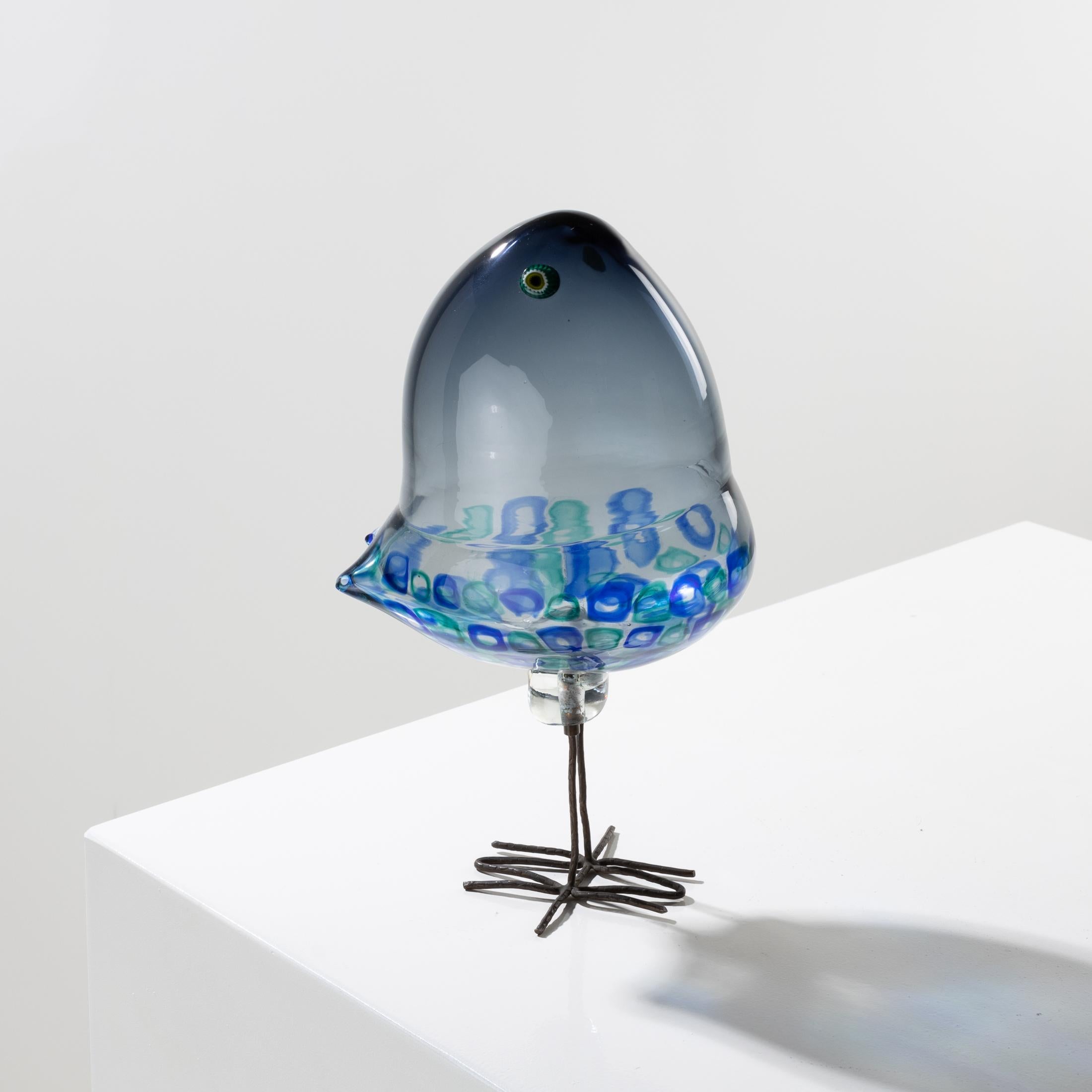 Glass bird resting on its hammered copper legs, designed by Alessandro Pianon for Vistosi in Murano, in 1962.
Its dark gray glass body, which can sometimes turn to a beautiful blue, is decorated with green and blue square murrines arranged