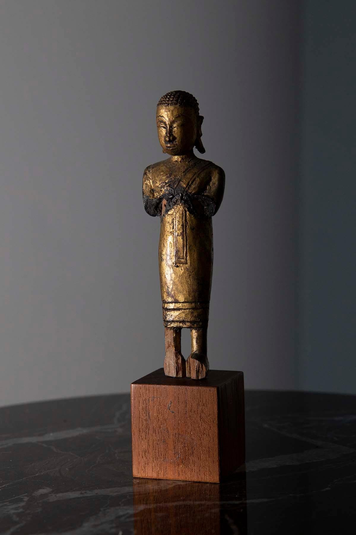 n the heart of 19th century Burma, an exquisite treasure of profound spiritual significance was born—a small, finely crafted sculpture of a Buddhist monk in prayer. This delicate work of art, lovingly hand-painted and gilded, embodies the timeless