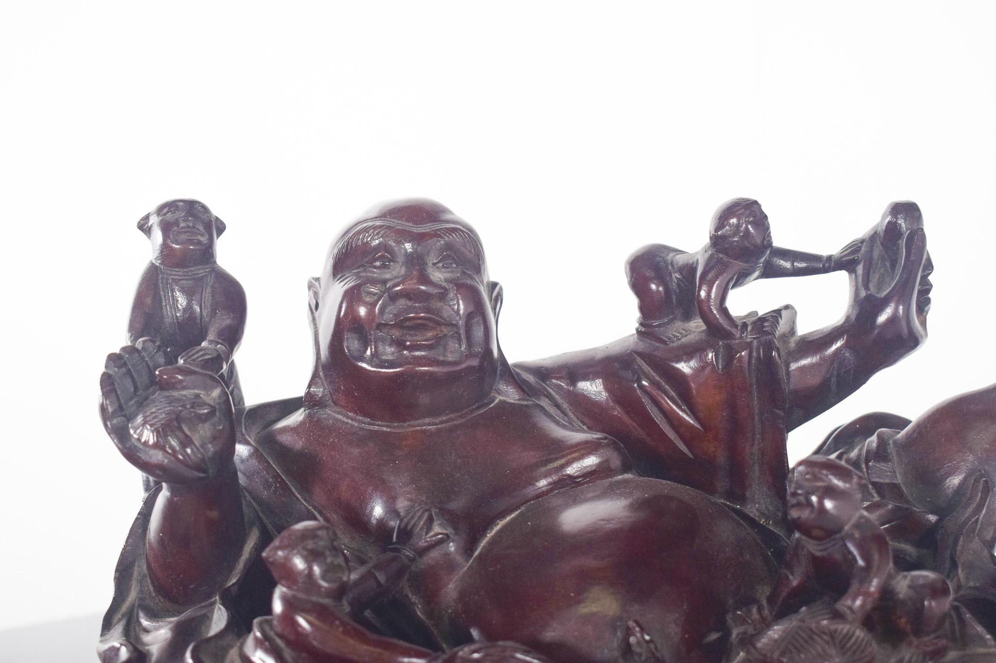 Scultura di budai in resina. La scultura mostra il personaggio, Budai, sdraiato in modo rilassato, con un'espressione gioviale e un ventre prominente, circondato da diverse scimmie e un serpente che interagiscono con il suo corpo e le sue