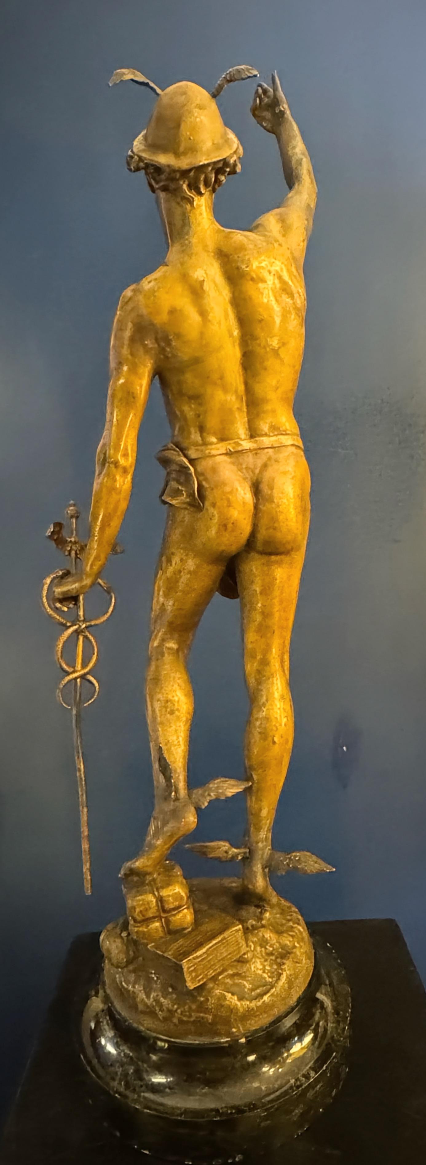 La pieza capta la esencia del dios romano con una pose dinámica y elegante, mostrando su agilidad y elocuencia.
La figura de Mercurio se presenta con el brazo derecho extendido hacia arriba, gesto que sugiere una orden o un saludo, mientras que el
