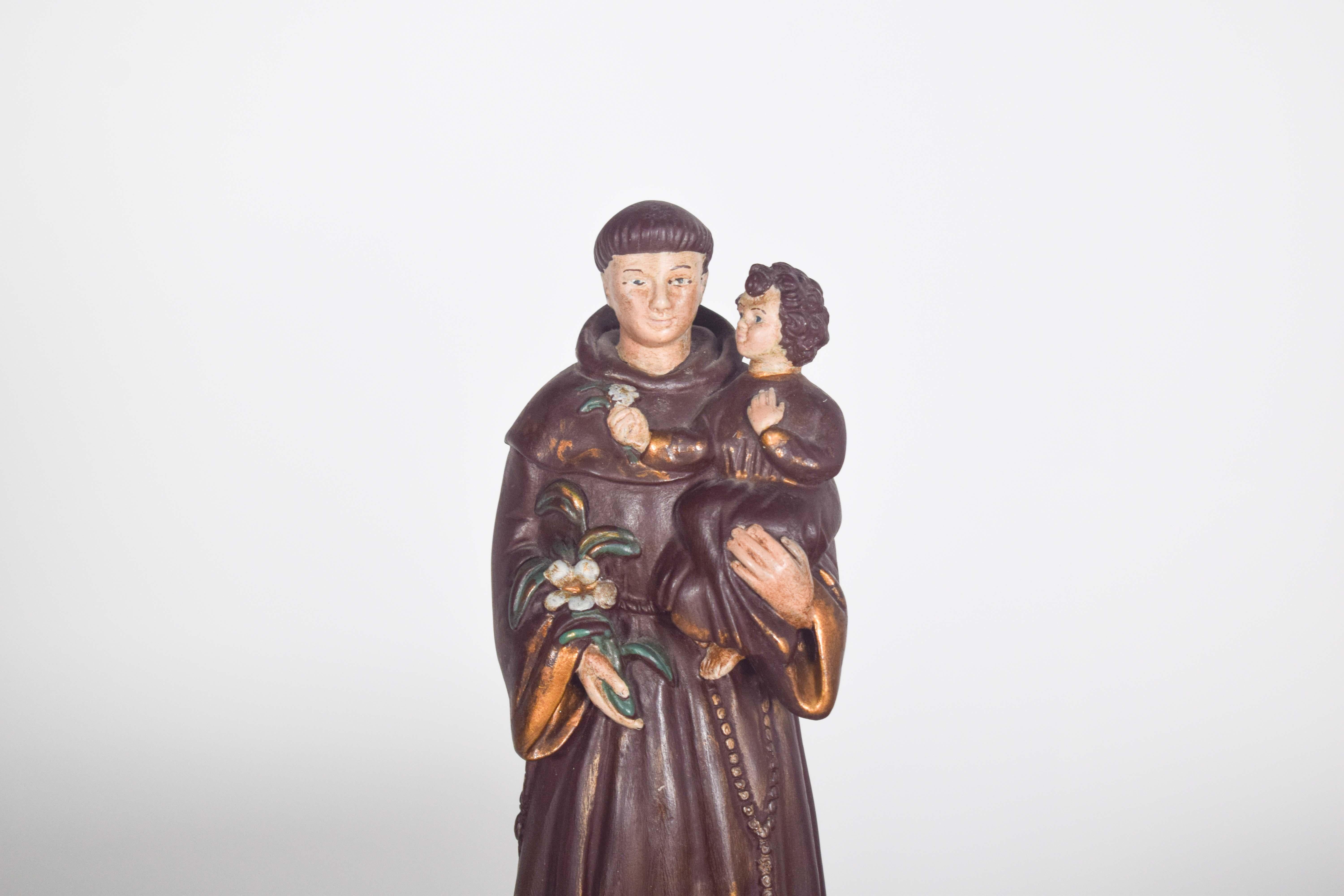 This ceramic sculpture of Saint Anthony with the Child is a beautifully crafted representation of devotion and purity. The figure stands tall, captured in a serene and gentle pose. Saint Anthony is dressed in a simple brown habit, with a cord tied