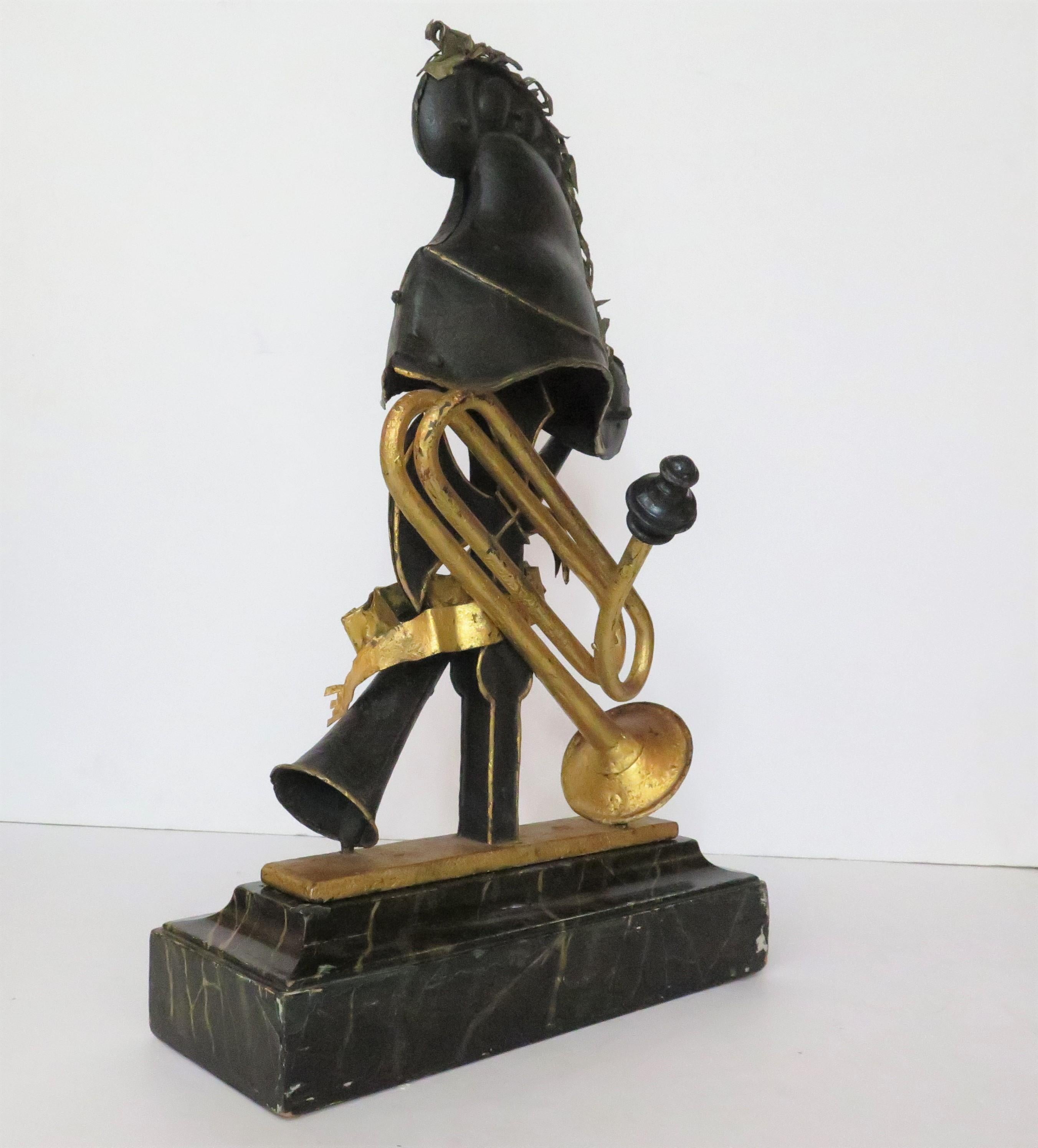 a French sculpture, paint and parcel gilt metal, of a Phrygian helmet (with gilt details) including gilt feather trim, on a halberd, with crossed horn and a gold trumpet, a gilt ribbon 