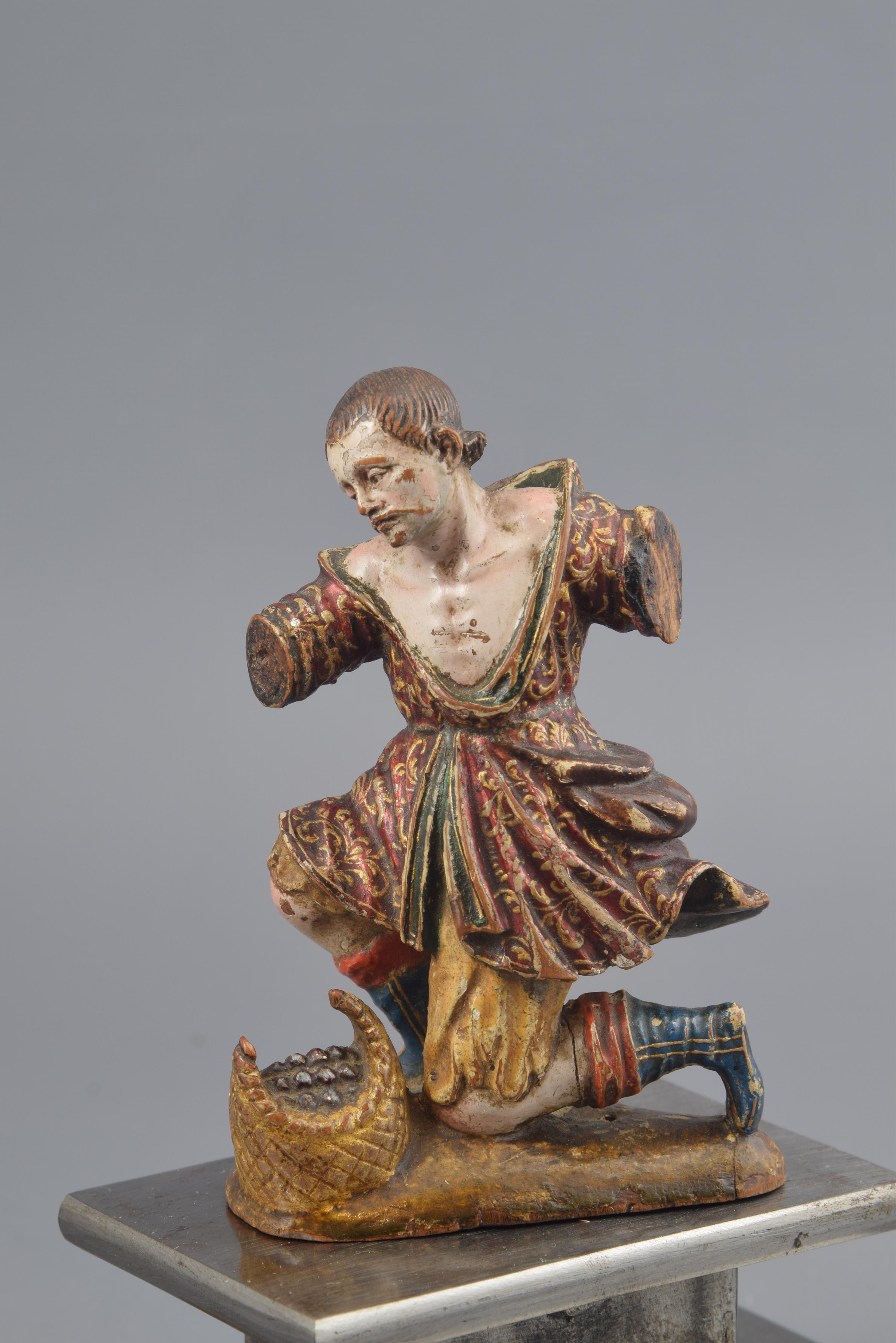 The male figure is place with a knee on the ground, slightly raised in an oval base in which also appears a basket with something inside. The boy, young, is dressed in a short tunic (that has a certain movement in its folds, and with a delicate