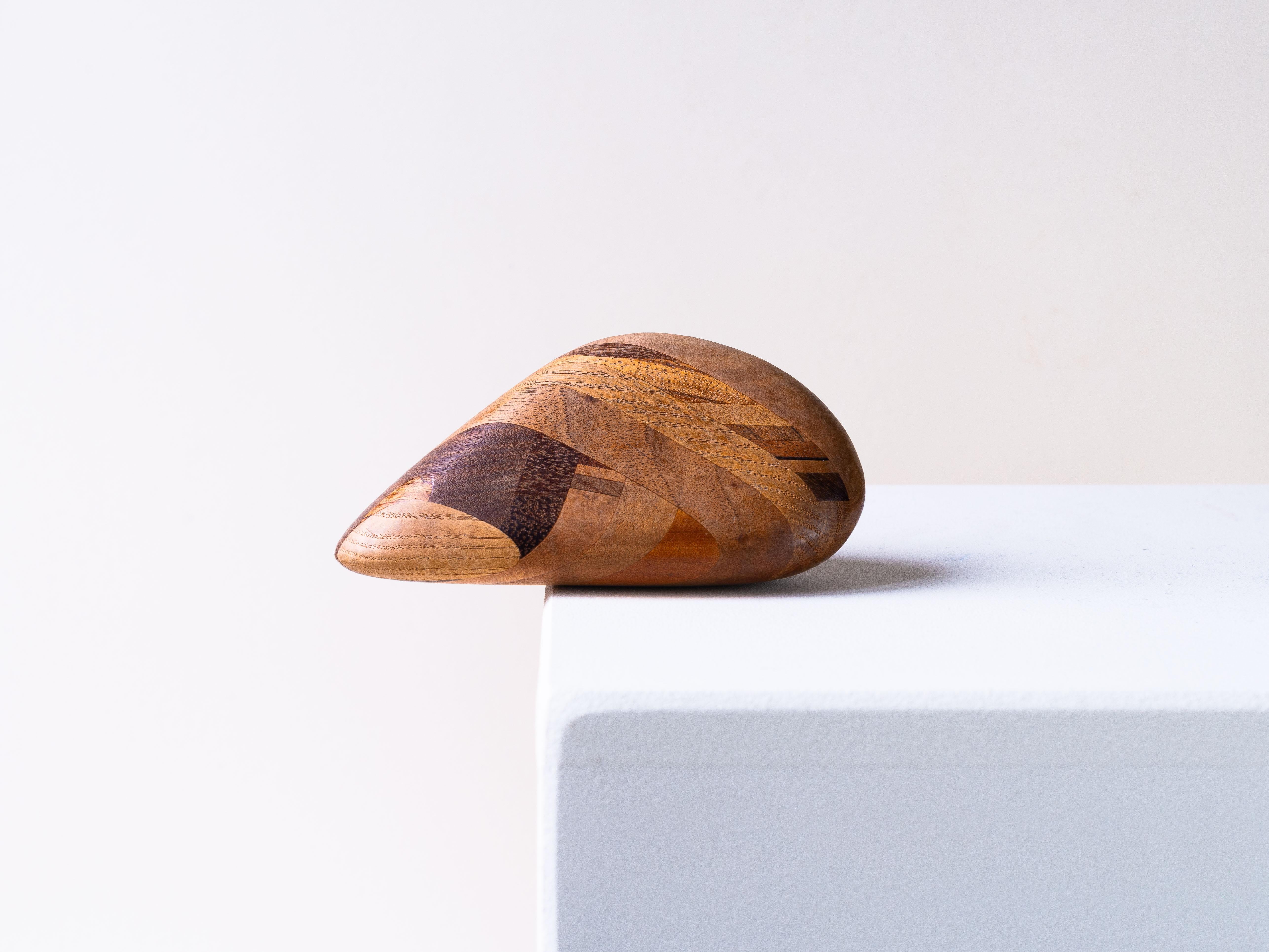 Wooden paperweight or decorative pebble sculpture.

From Denmark dating back to the 1970s.

The object is crafted from an assembly of different wood species. It employs a technique reminiscent of marquetry, but here it involves solid wood pieces