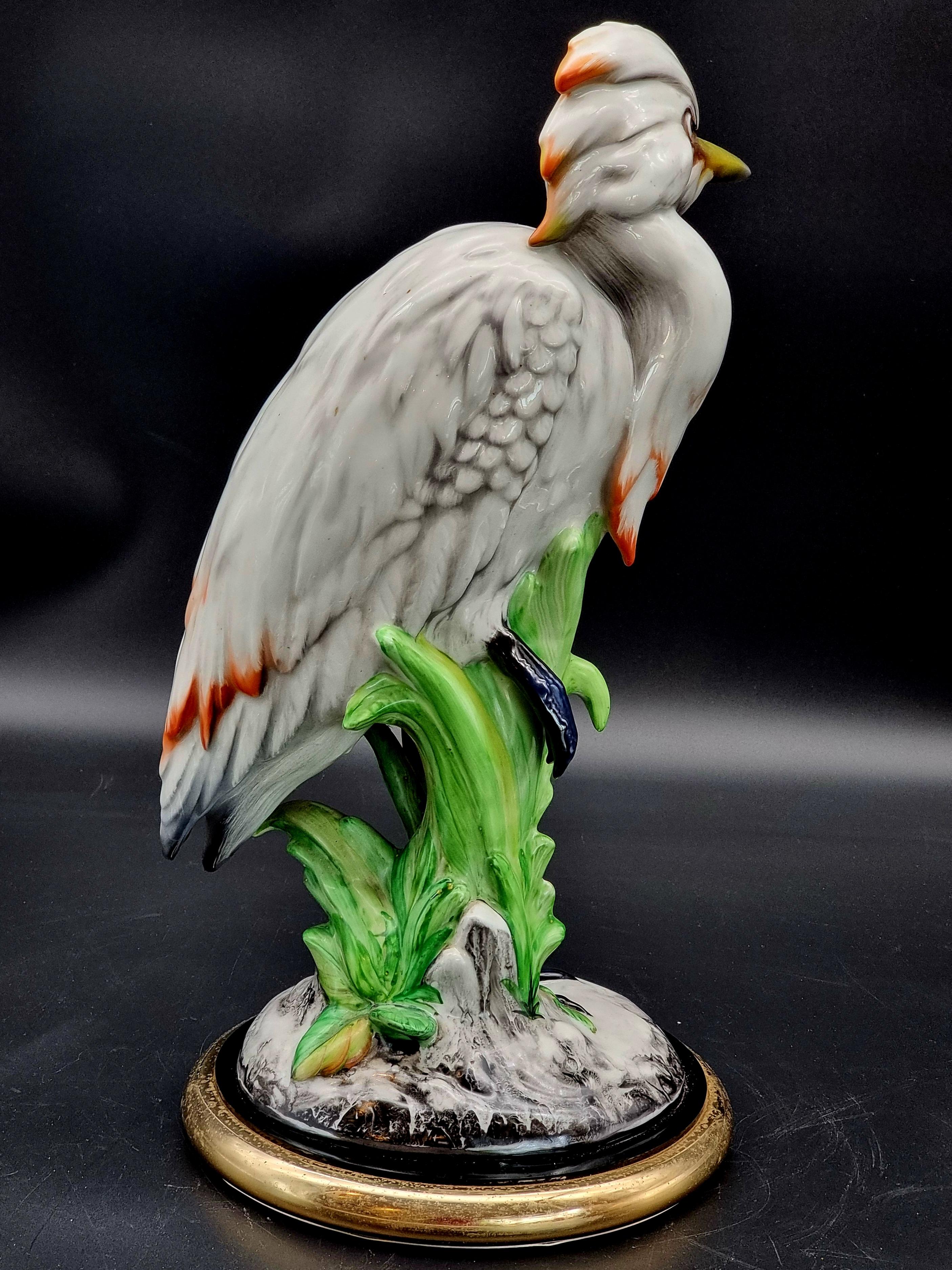 Scultura in ceramica smaltata raffigurante un elegante uccello marino, probabilmente un airone o un'egretta, eseguita con grande cura dei dettagli e realizzata intorno agli anni Cinquanta. L’uccello è raffigurato su una base decorata da foglie