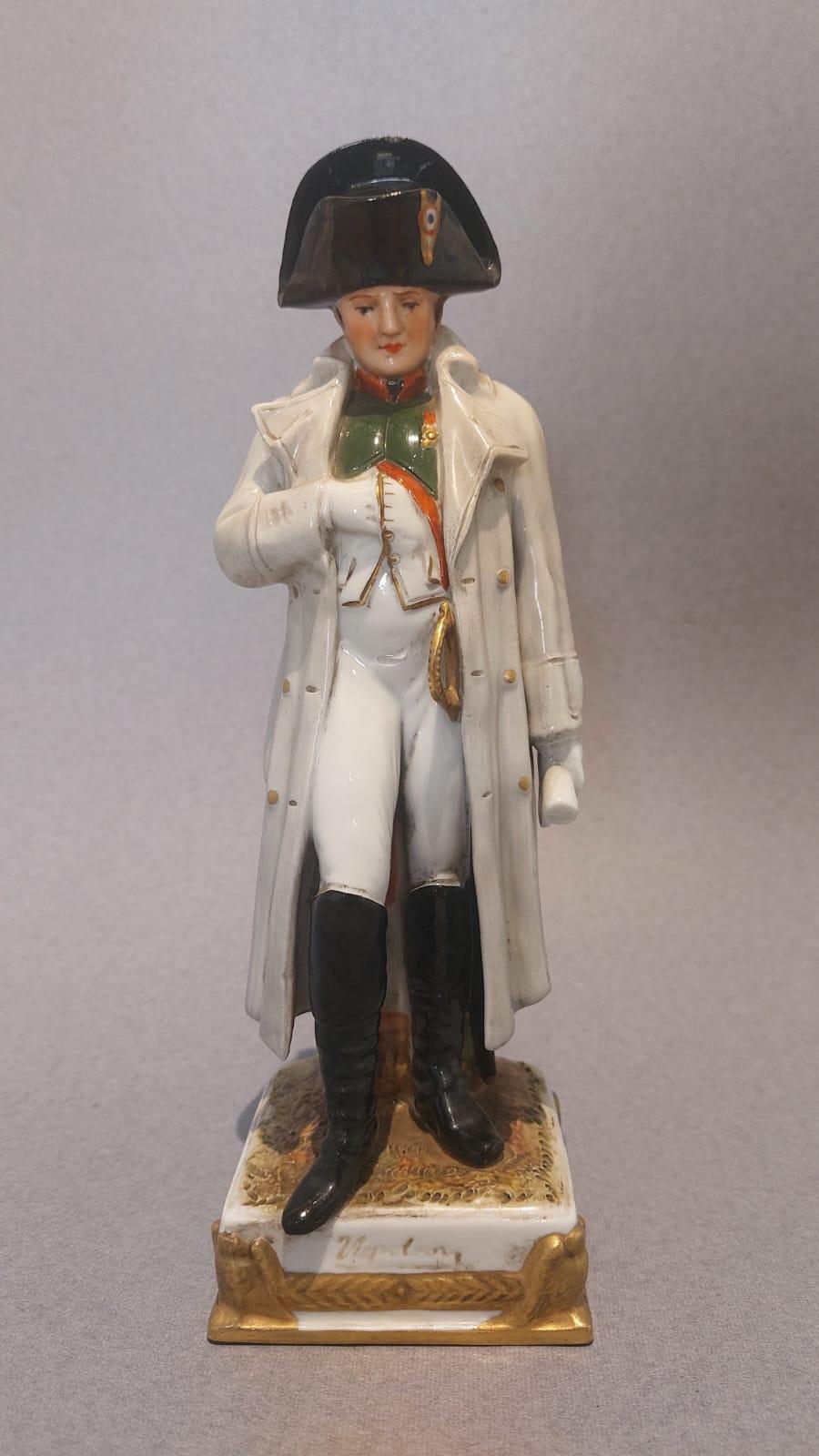 La sculpture en céramique représente Napoléon dans sa célèbre iconographie : il porte sa coiffe classique, son costume typique qui descend le long du corps, son pantalon de toile ajusté qui se termine par de hautes bottes noires et le gilet dans
