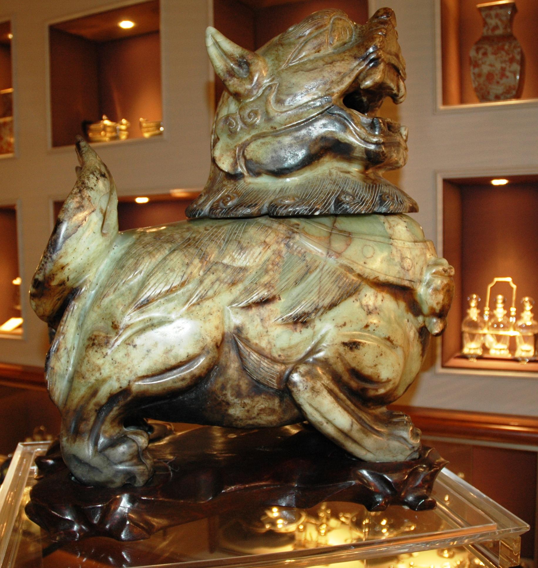 Undergrowth green color jade sculpture depicting a Fo dog. It rests on a shaped wooden base. The sculpture consists of only two jade blocks, the head and body, with a total weight of about one quintal. The head is movable and detachable from the