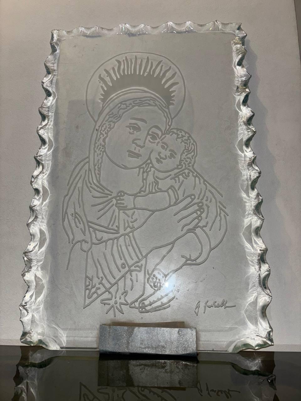 Questa scultura d'arte in vetro martellato e inciso cattura l'essenza della maternità con delicata maestria. La superficie frastagliata del vetro martellato crea un dinamico gioco di luci e ombre, esaltando la tenera incisione della Madonna che