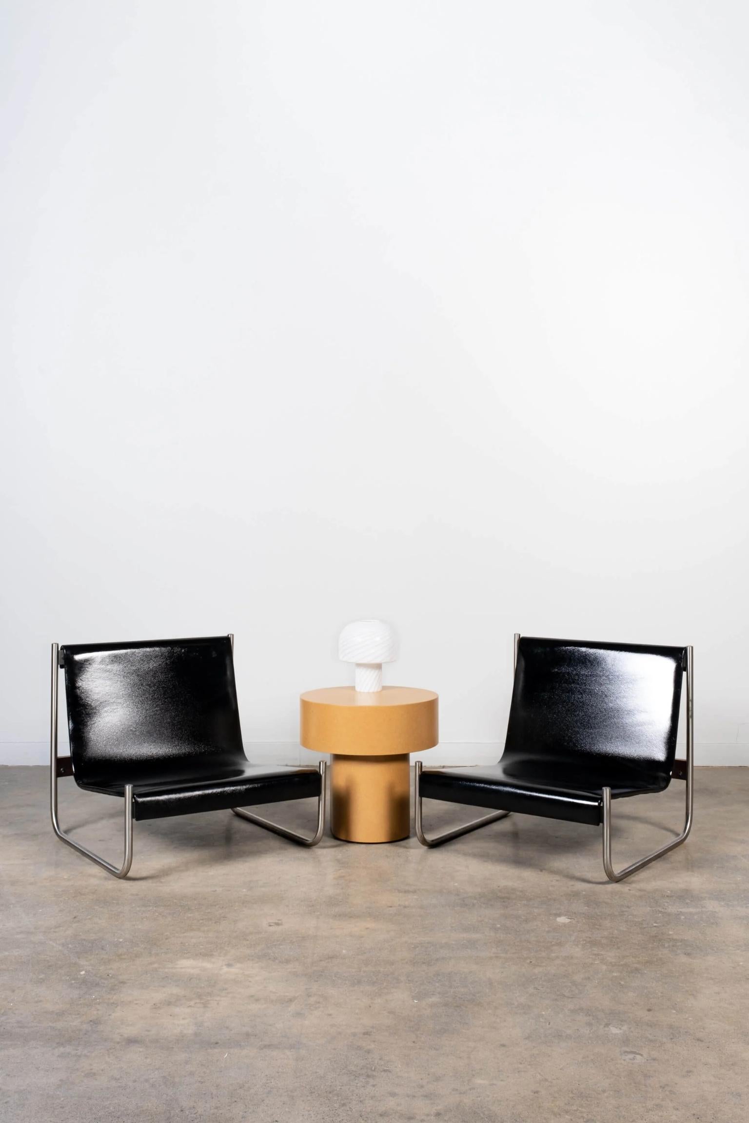 Slick black patent leather stretched over a chrome base, provides cool comfort on the pair of Scuola di Torino lounge chairs. The low-profile armless leather sling chairs are sold as a pair.